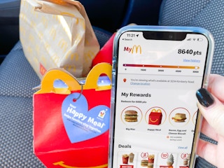person holding phone with mcdonalds app next to happy meal