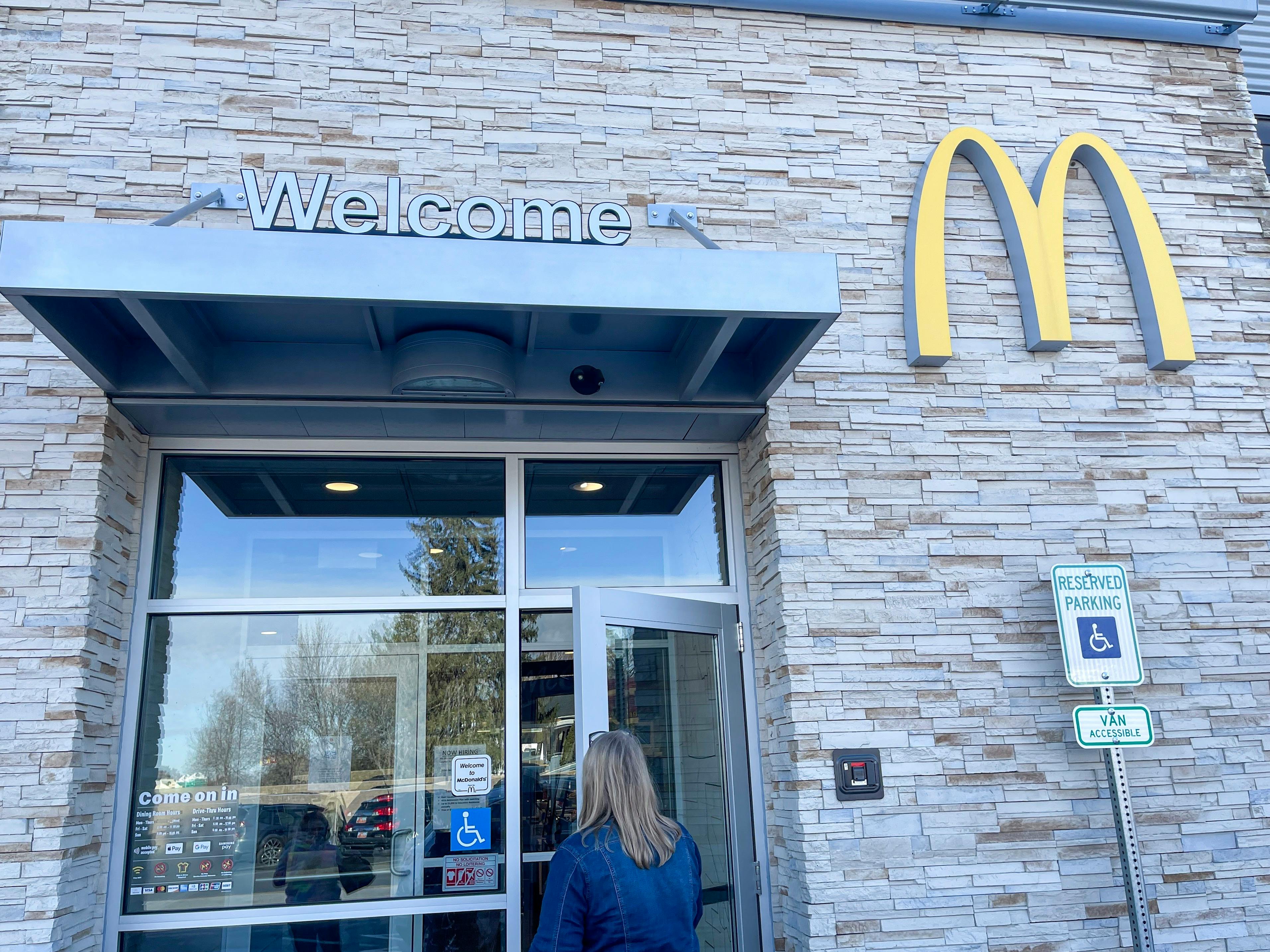 A person walking in the entrance to McDonald's with a "Welcome" sign above the door and the golden arches logo on the building's exterior.
