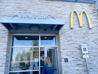 A person walking in the entrance to McDonald's with a "Welcome" sign above the door and the golden arches logo on the building's exterior.