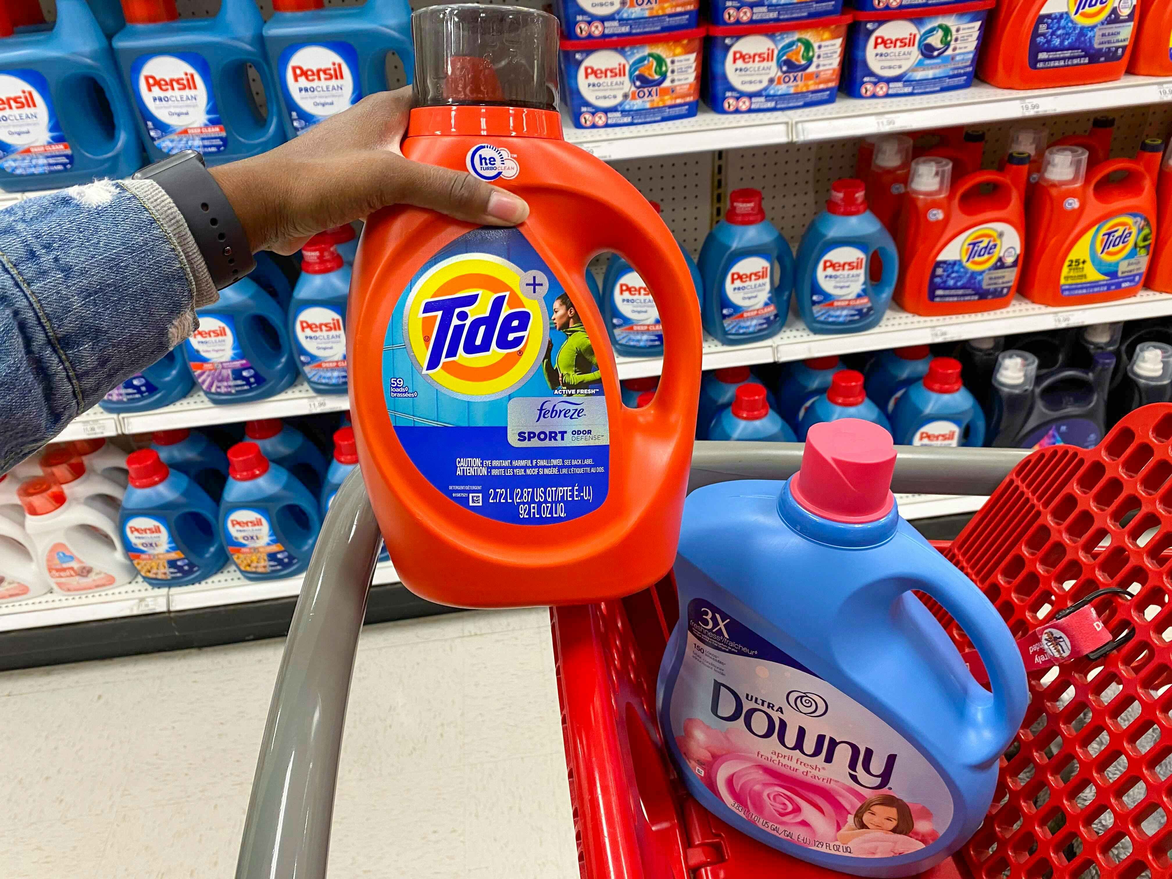 hand holding up Tide detergent over Target shopping cart that has a bottle of Downy in it