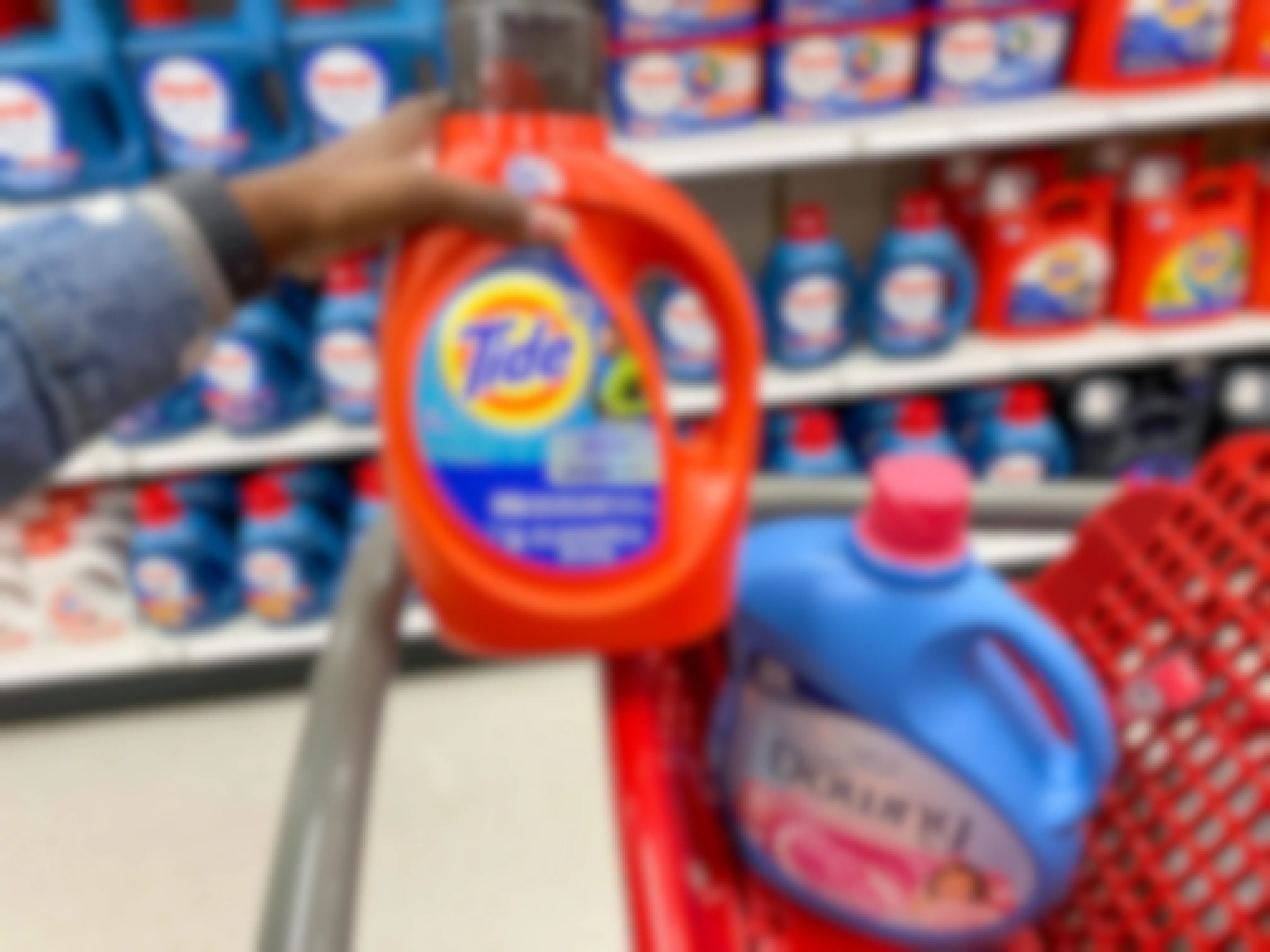 hand holding up Tide detergent over Target shopping cart that has a bottle of Downy in it