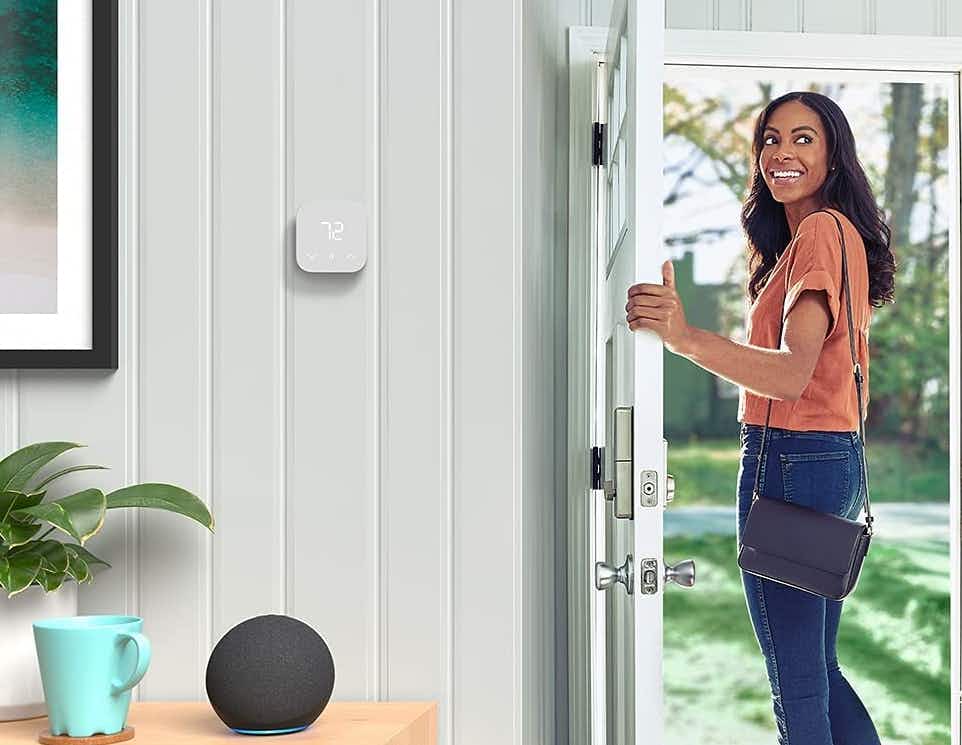 A woman smiling near her Amazon thermostat.