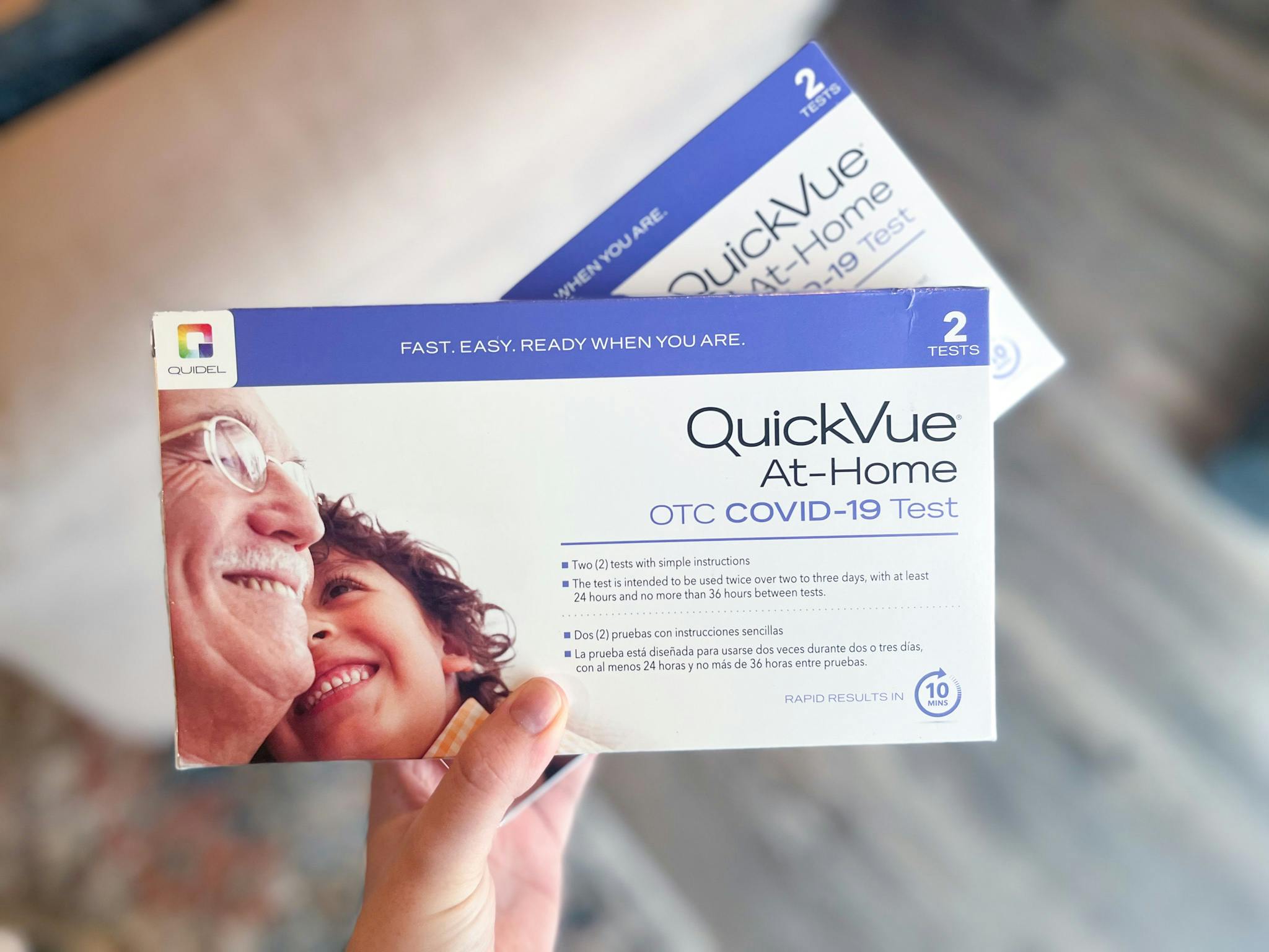 A person's hand holding up some QuickVue at-home COVID-19 test kits.