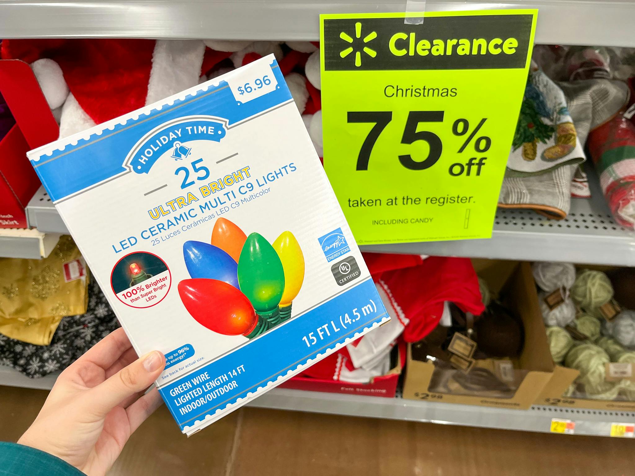 Someone holding a box of Holiday Time ultra bright LED ceramic multi colored Christmas string lights in front of a 75% off clearance sign