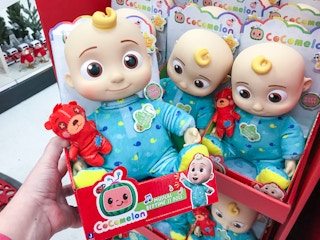 Someone holding a CoComelon Official Bedtime JJ Doll in front of a shelf of more dolls.