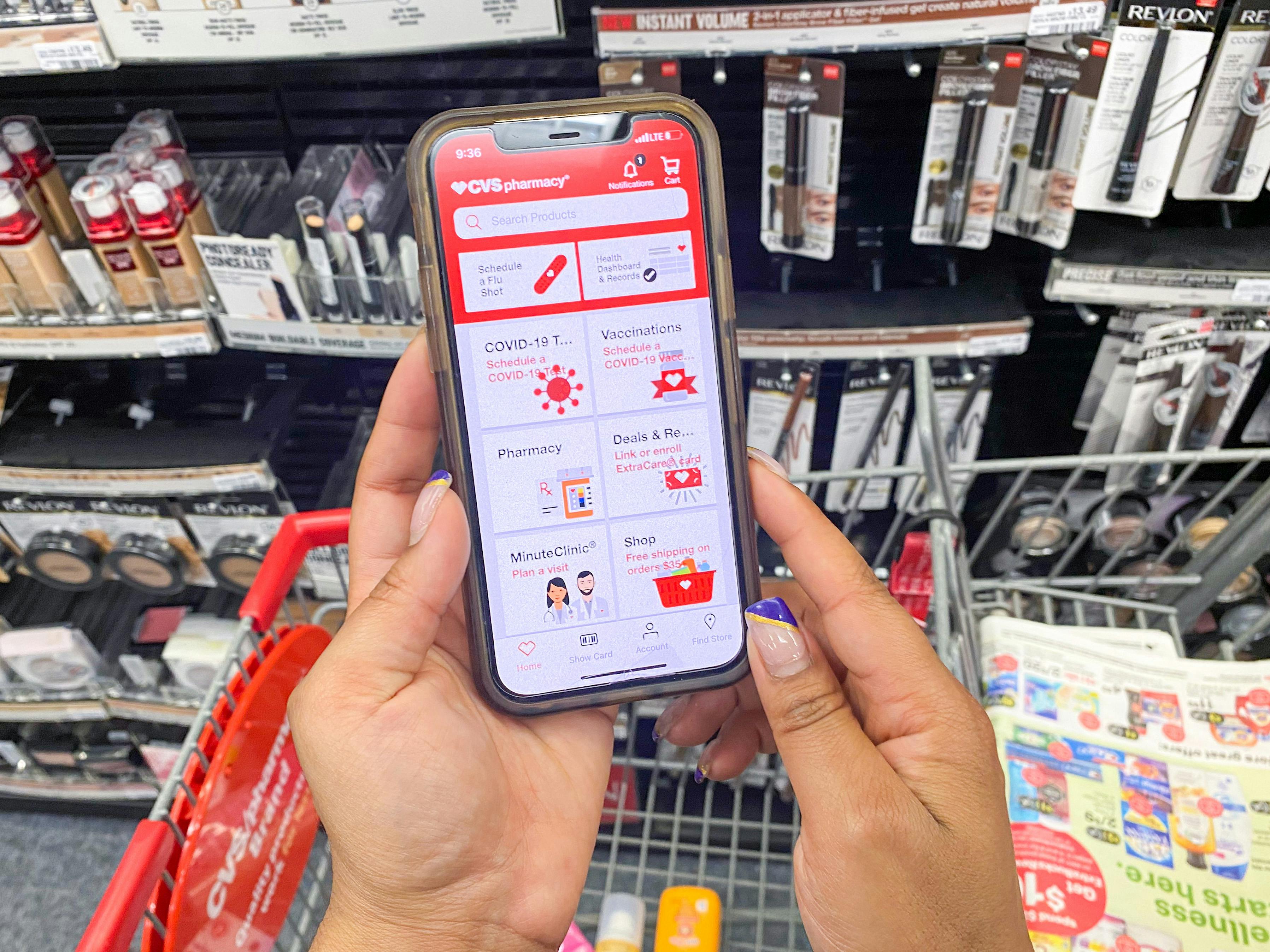 a woman holding her phone and looking at the cvs pharmacy mobile app while standing in the makeup aisle of a CVS store