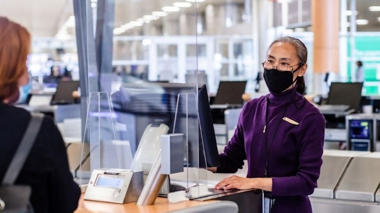 A person standing at a desk at an airport, talking to an employee.