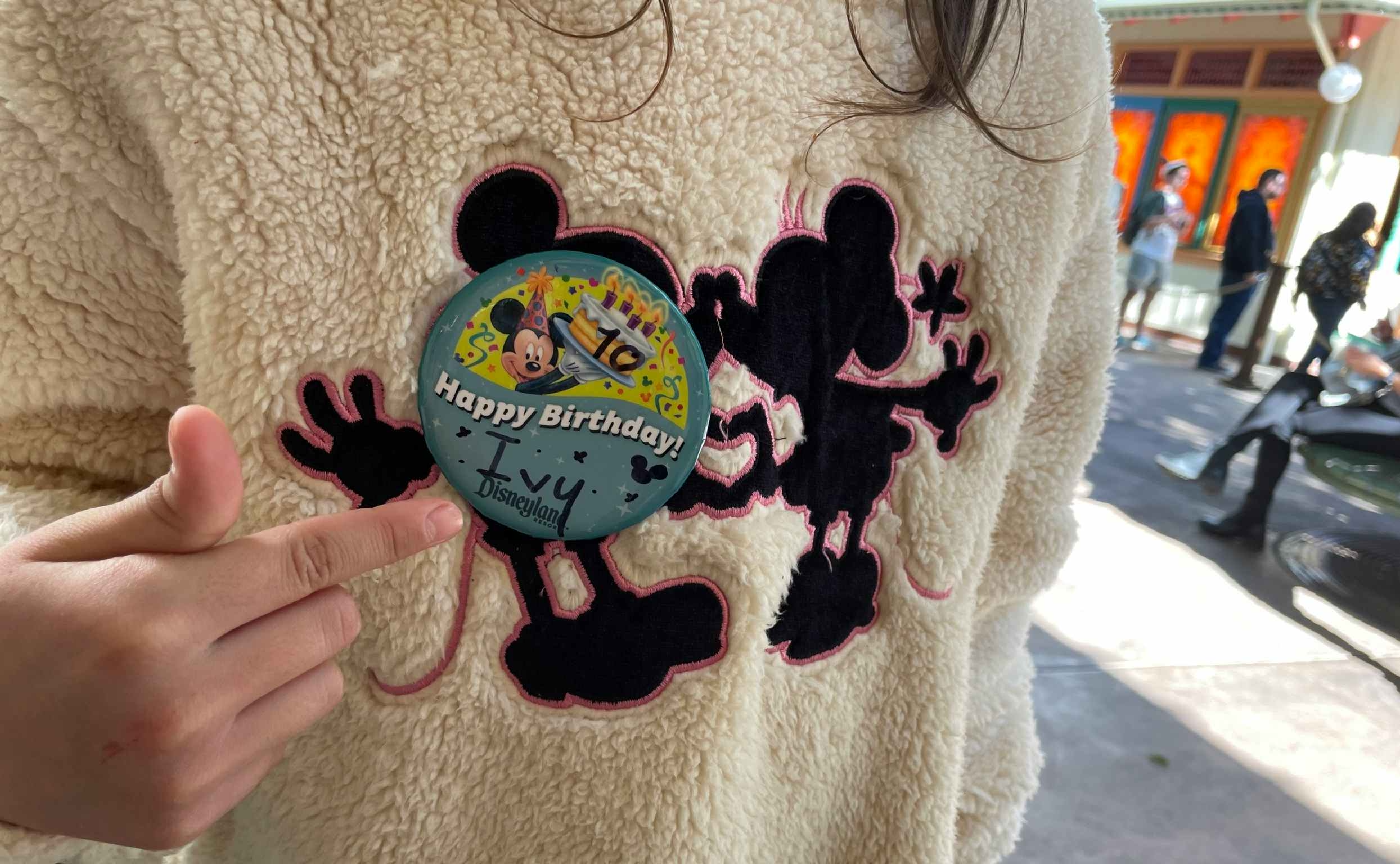 A close up of a Disney birthday button pinned on a child's Mickey and Minnie sweatshirt.