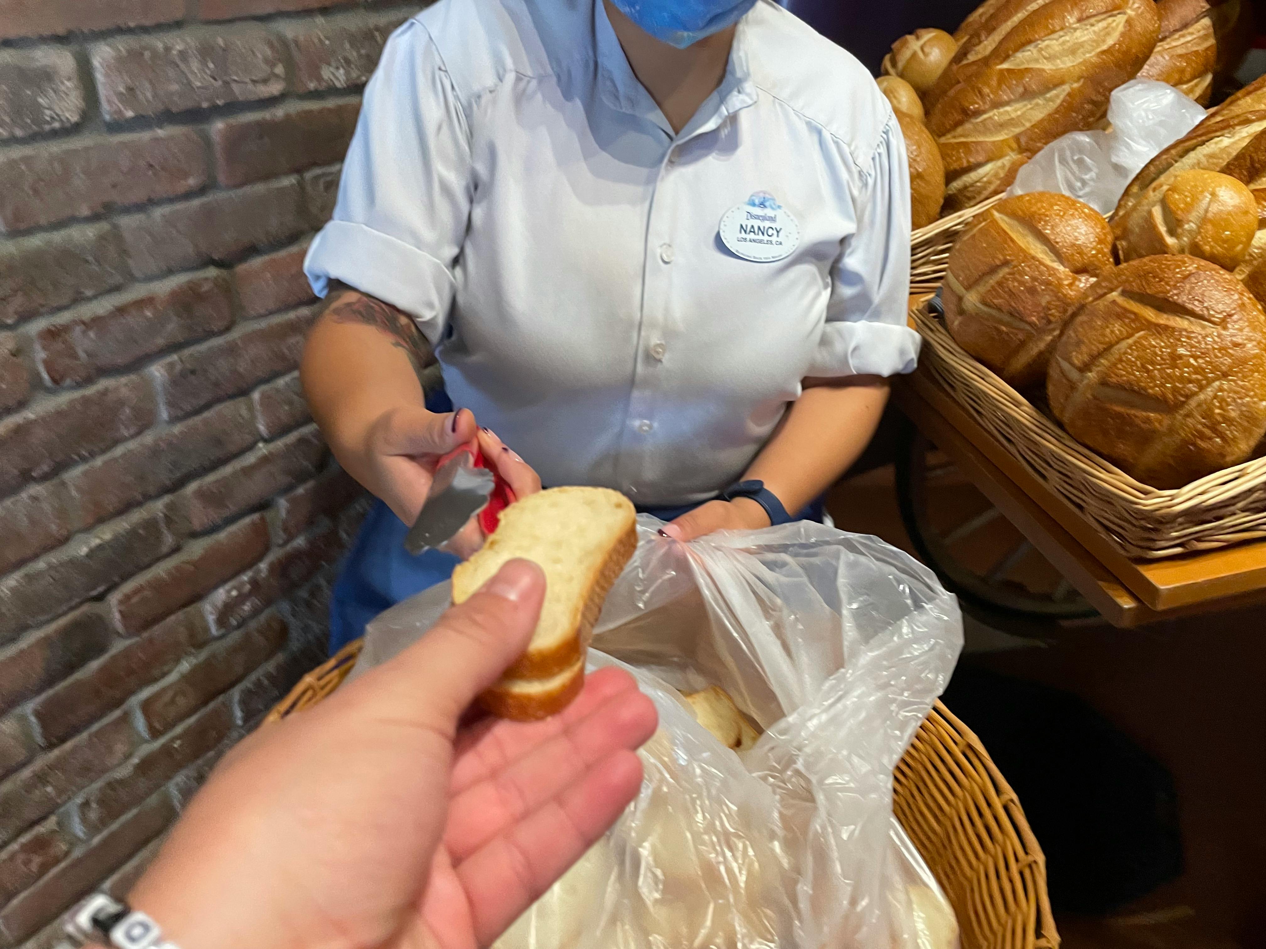 A Disney employee handing free bread to a patron in Boudoin Bakery at Disneyland.