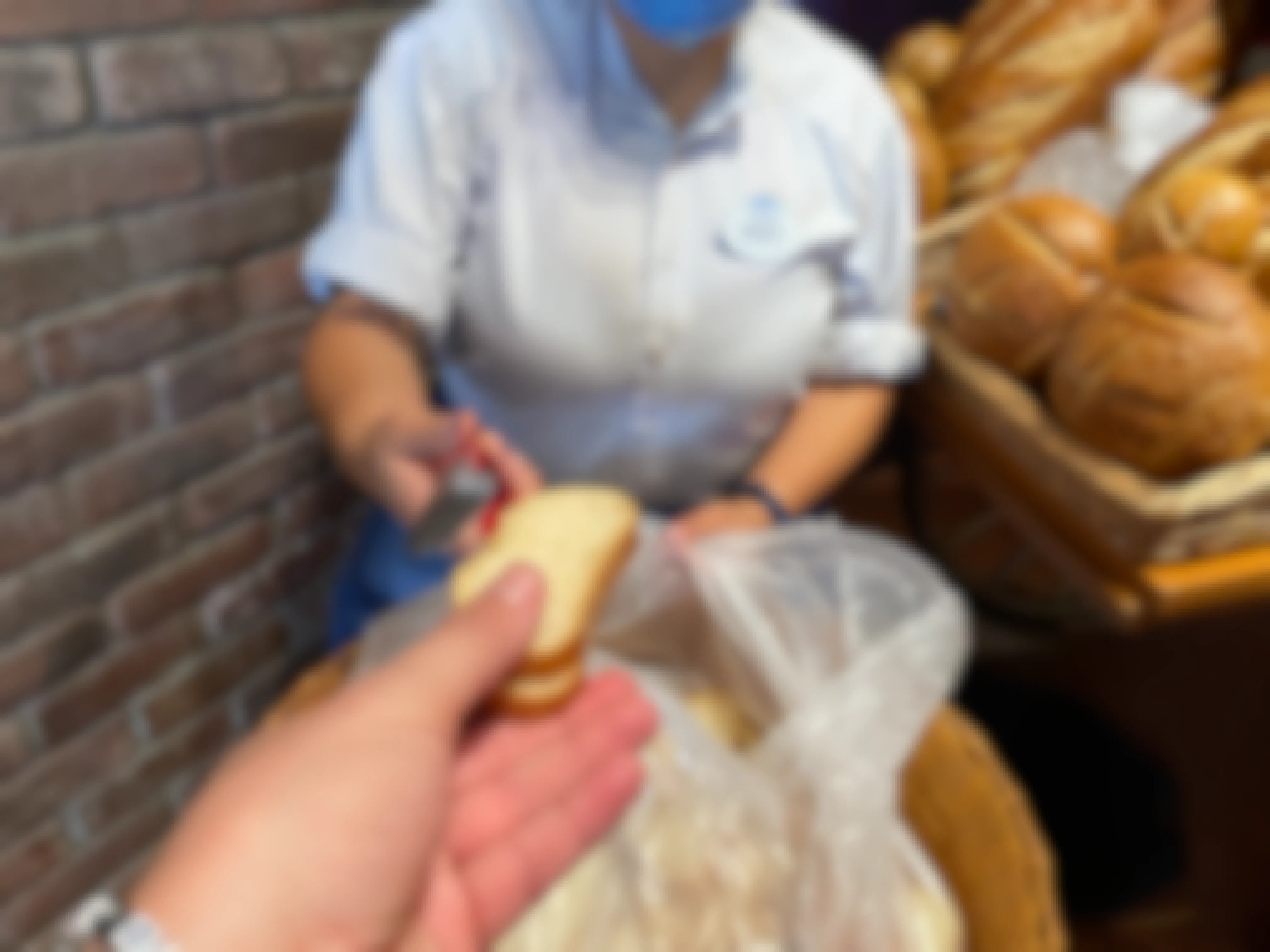 A Disney employee handing free bread to a patron in Boudoin Bakery at Disneyland.