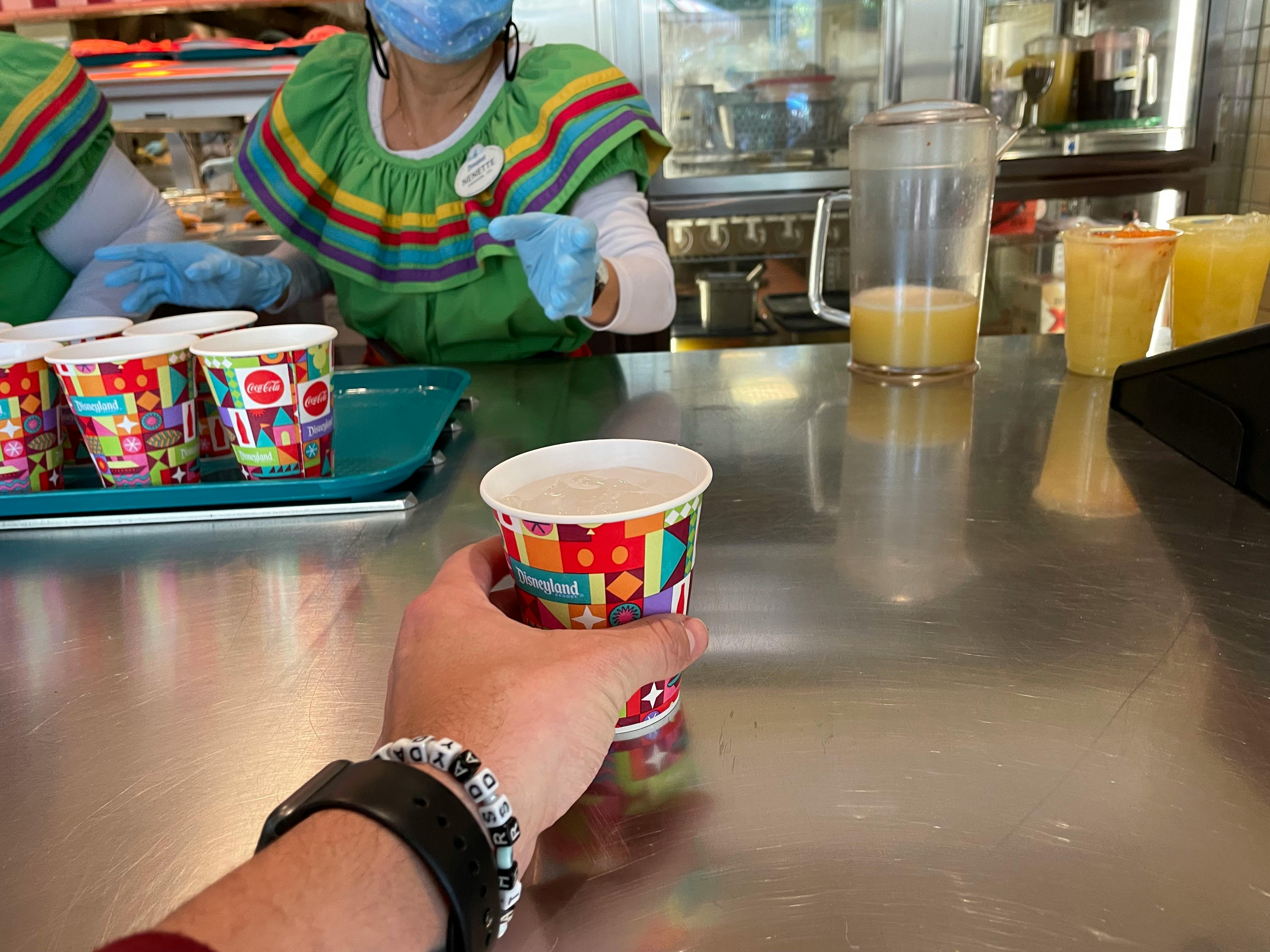 A person taking a free water cup from a counter inside a restaurant at Disneyland.