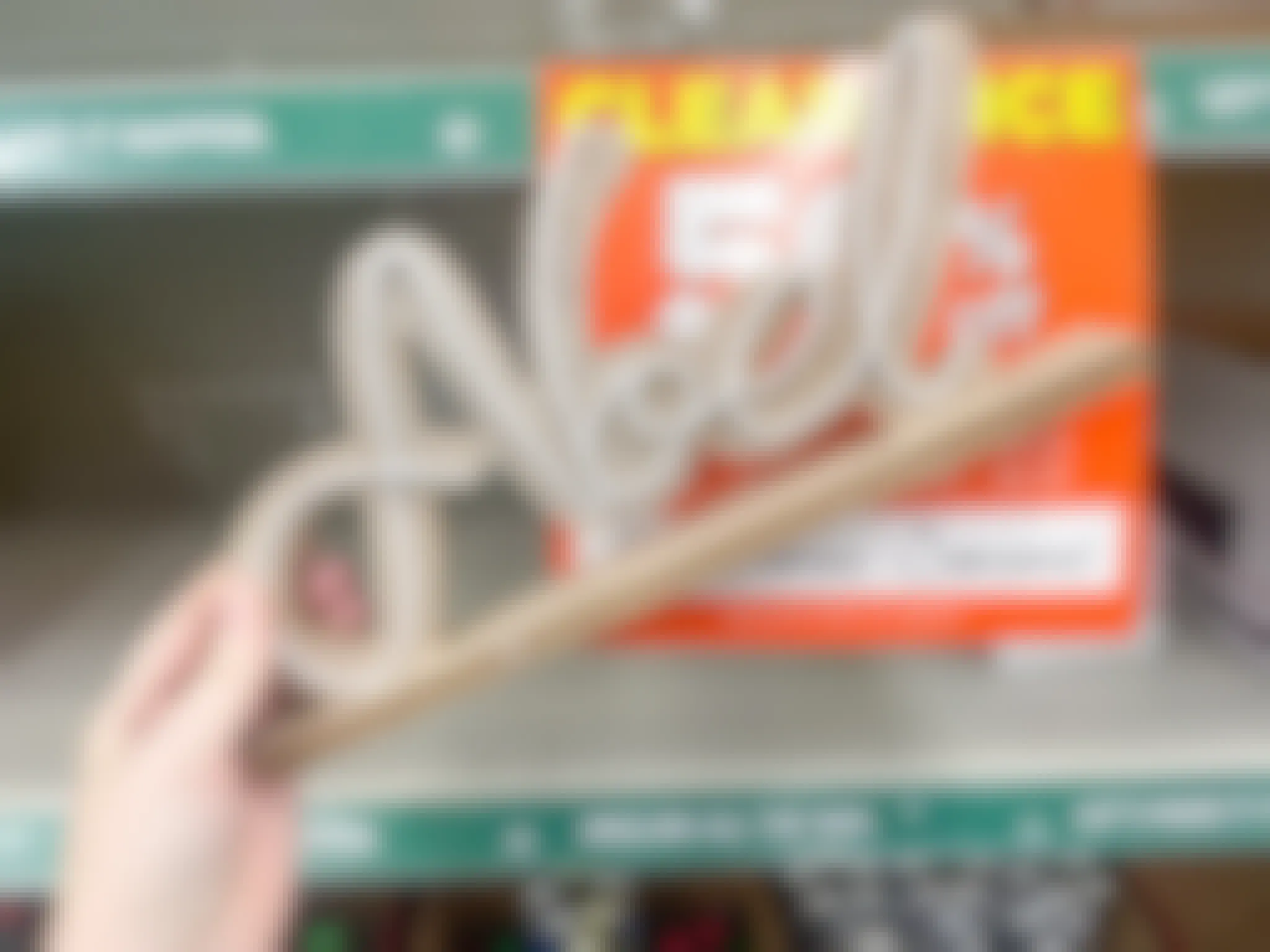 A person holding a Noel sign in front of a store shelf.