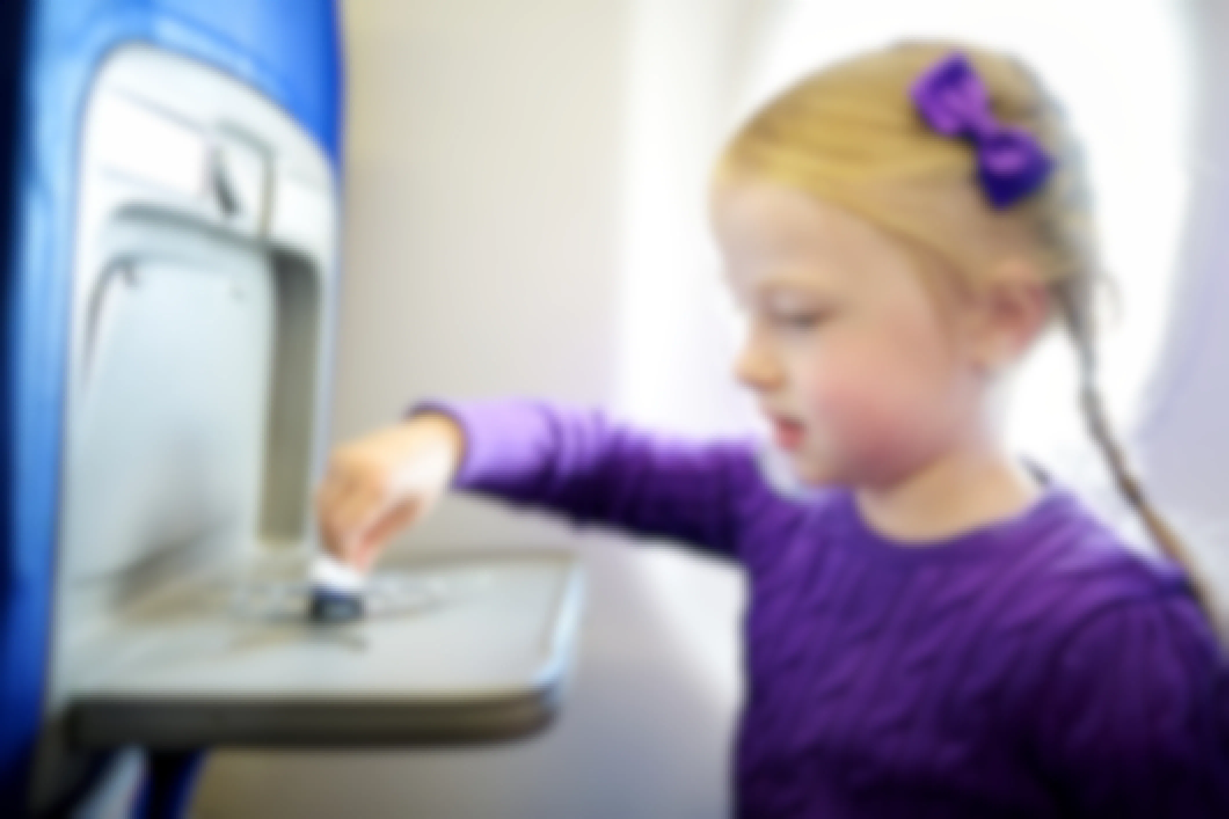 little girl sitting on a plane playing with a toy plane on the tray table