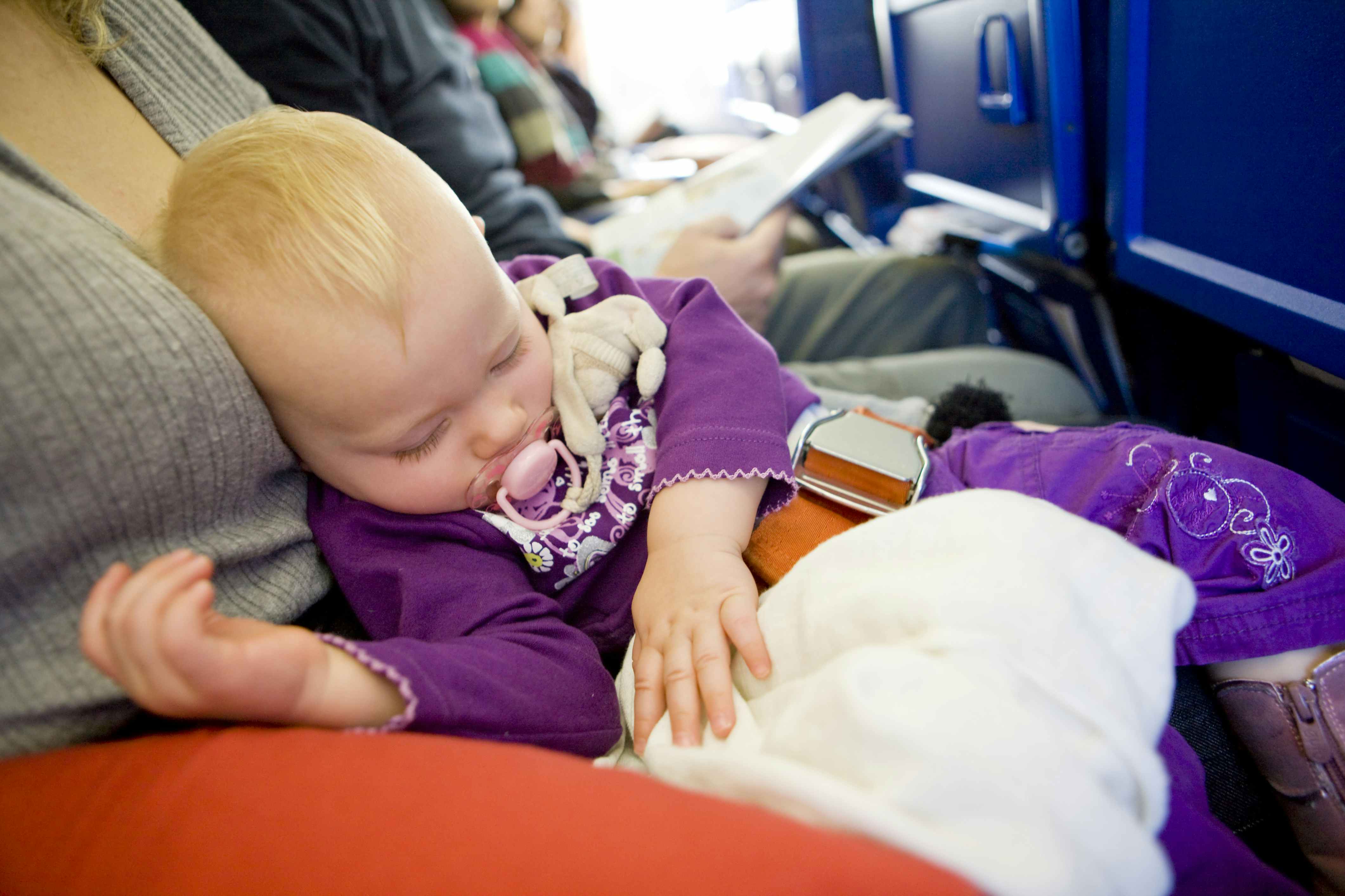 baby in a purple jumpsuit sleeping on mom's lap on a plane