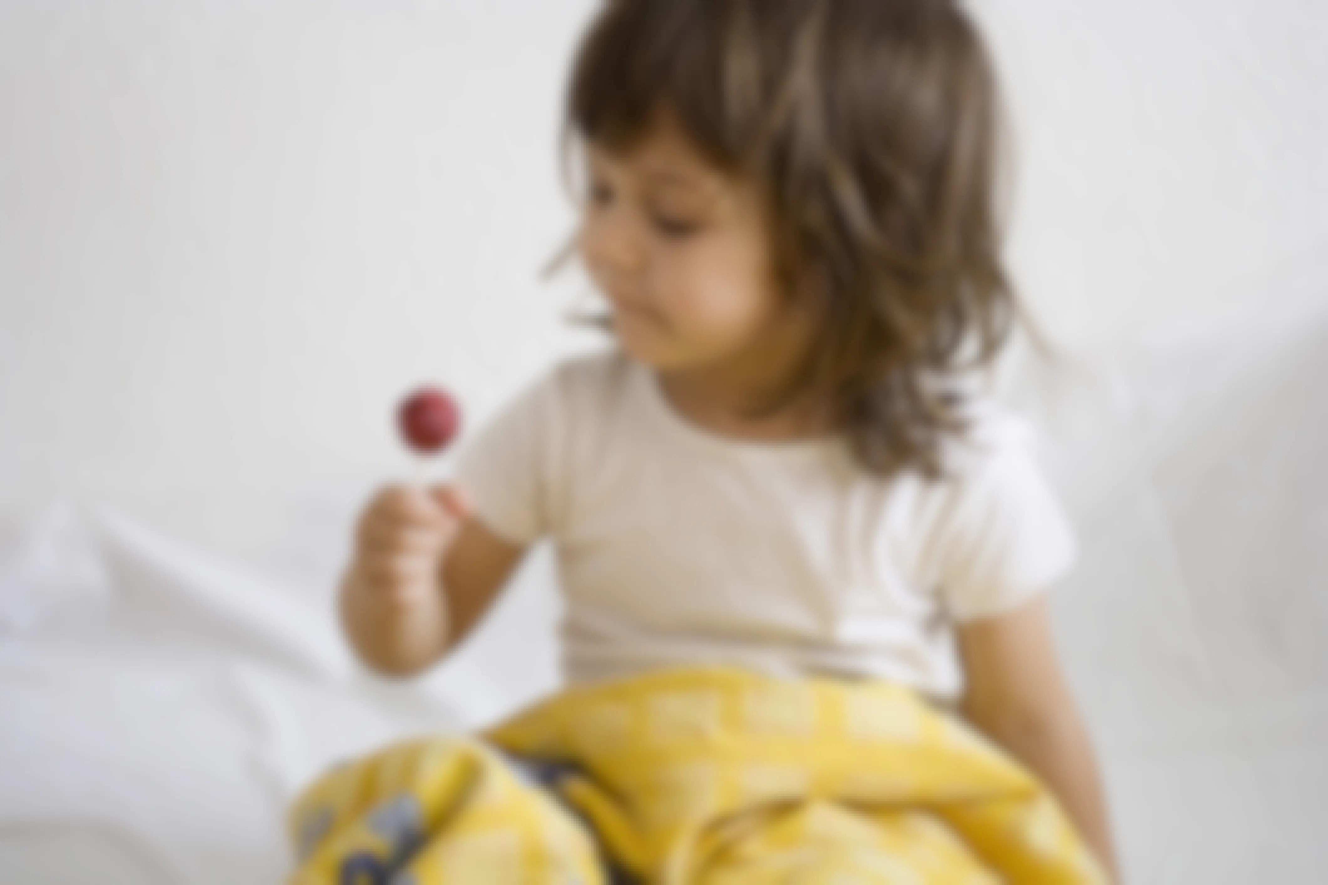 toddler sitting in bed eating a lollipop