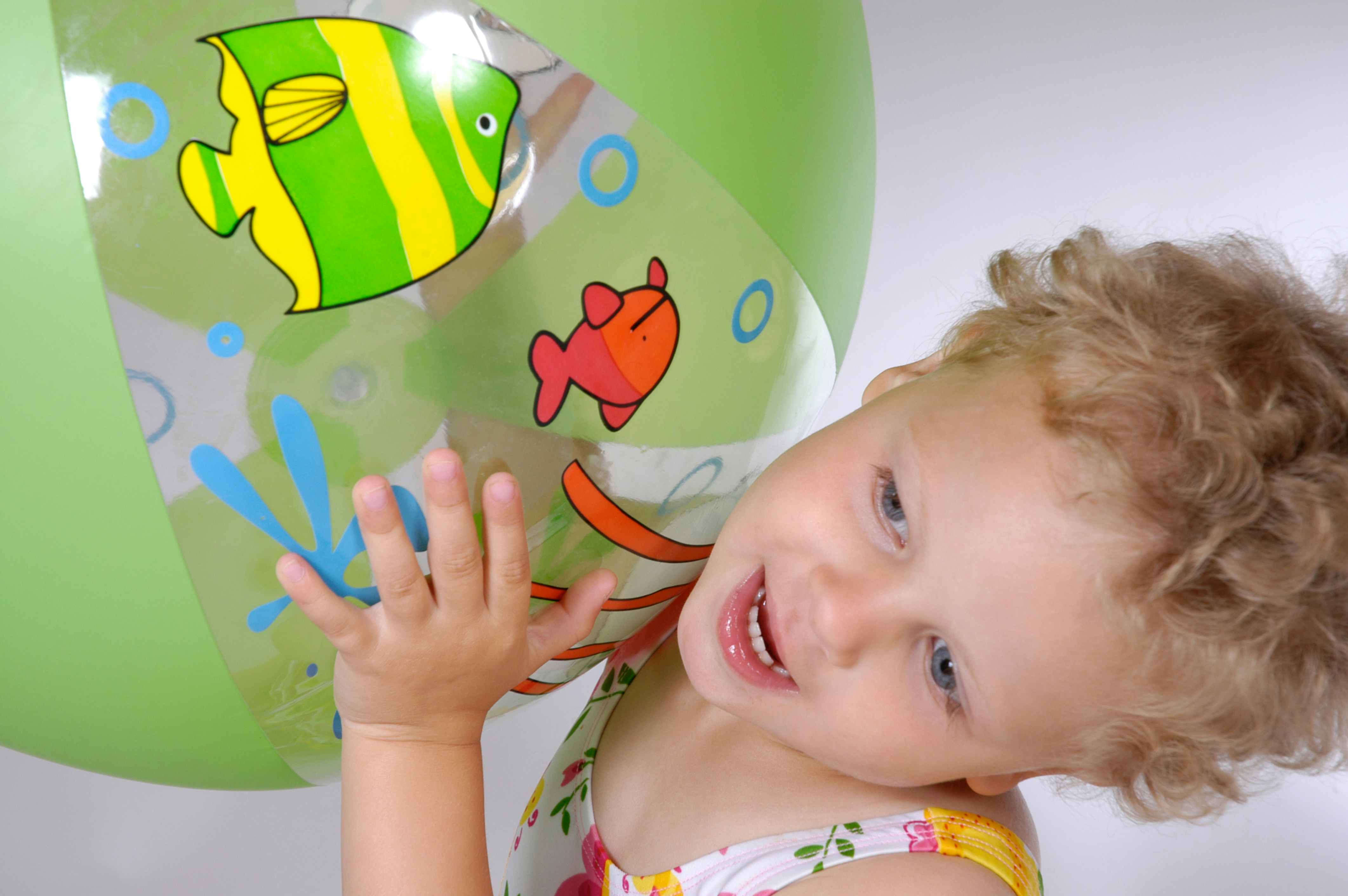 toddler girl holding up a green beach ball with fishes on it