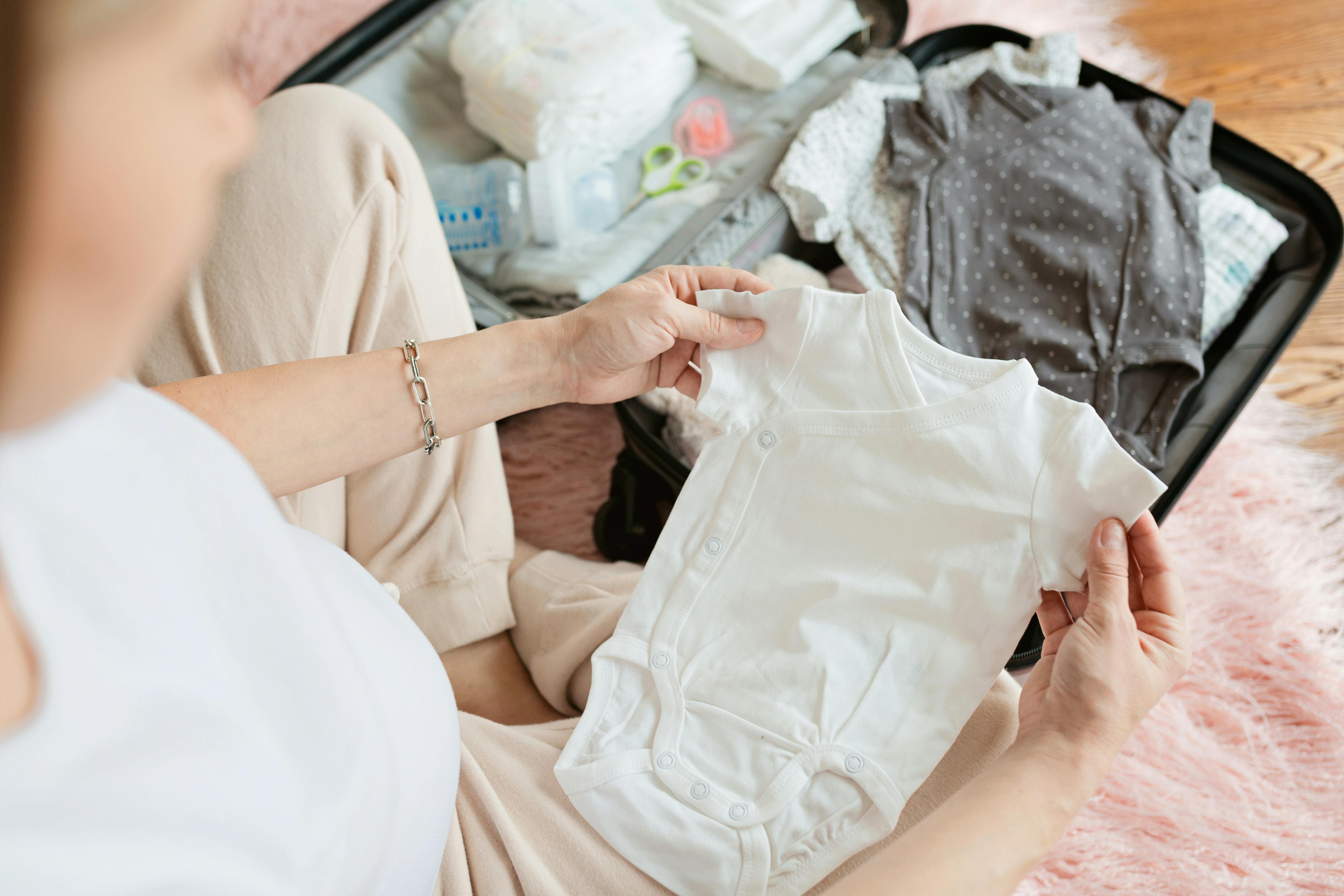 pregnant woman sitting on a shag rug packing baby clothes in a suitcase