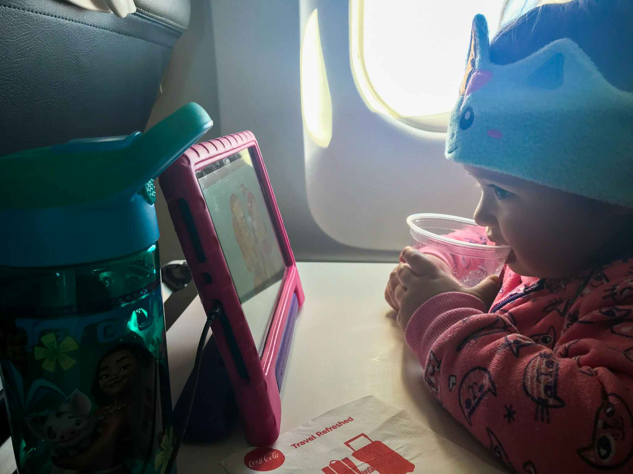 A kid watching a cartoon on an iPad while sitting in a seat on an airplane.