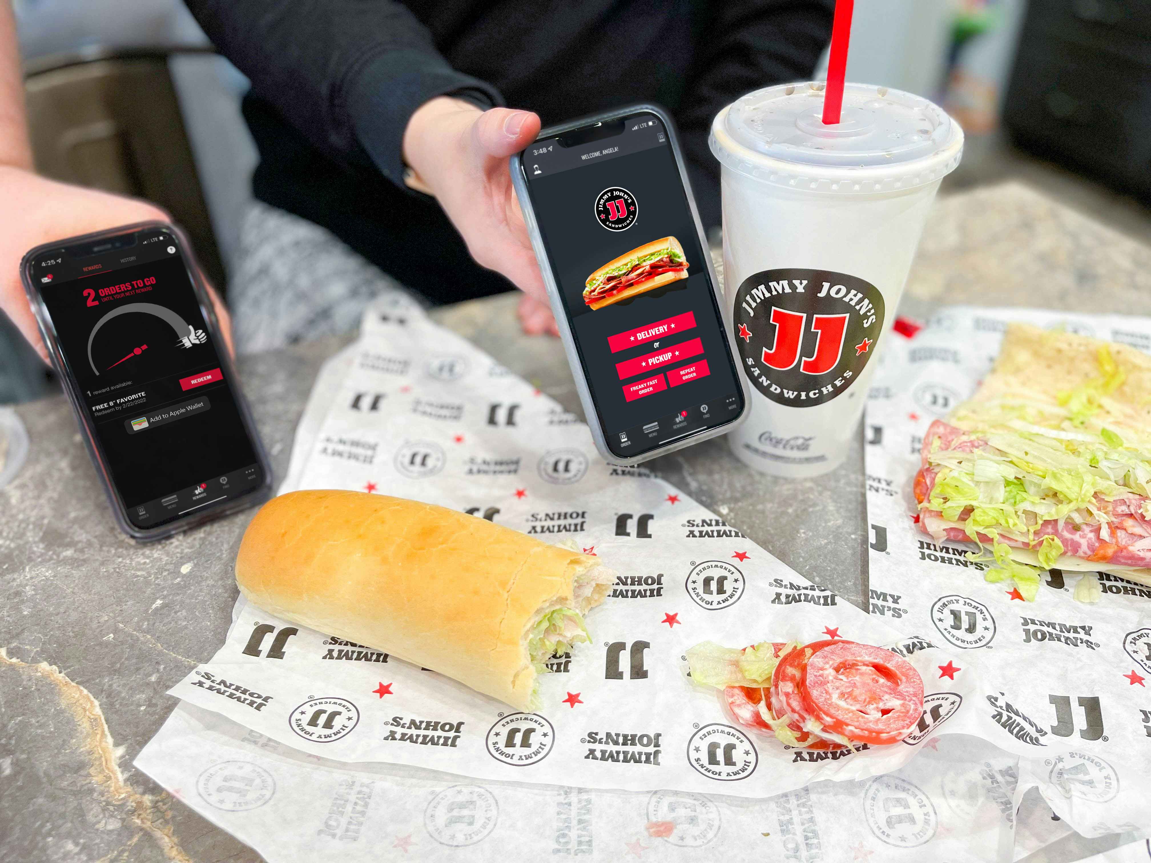 two hands holding phones with jimmy johns app with food on counter 