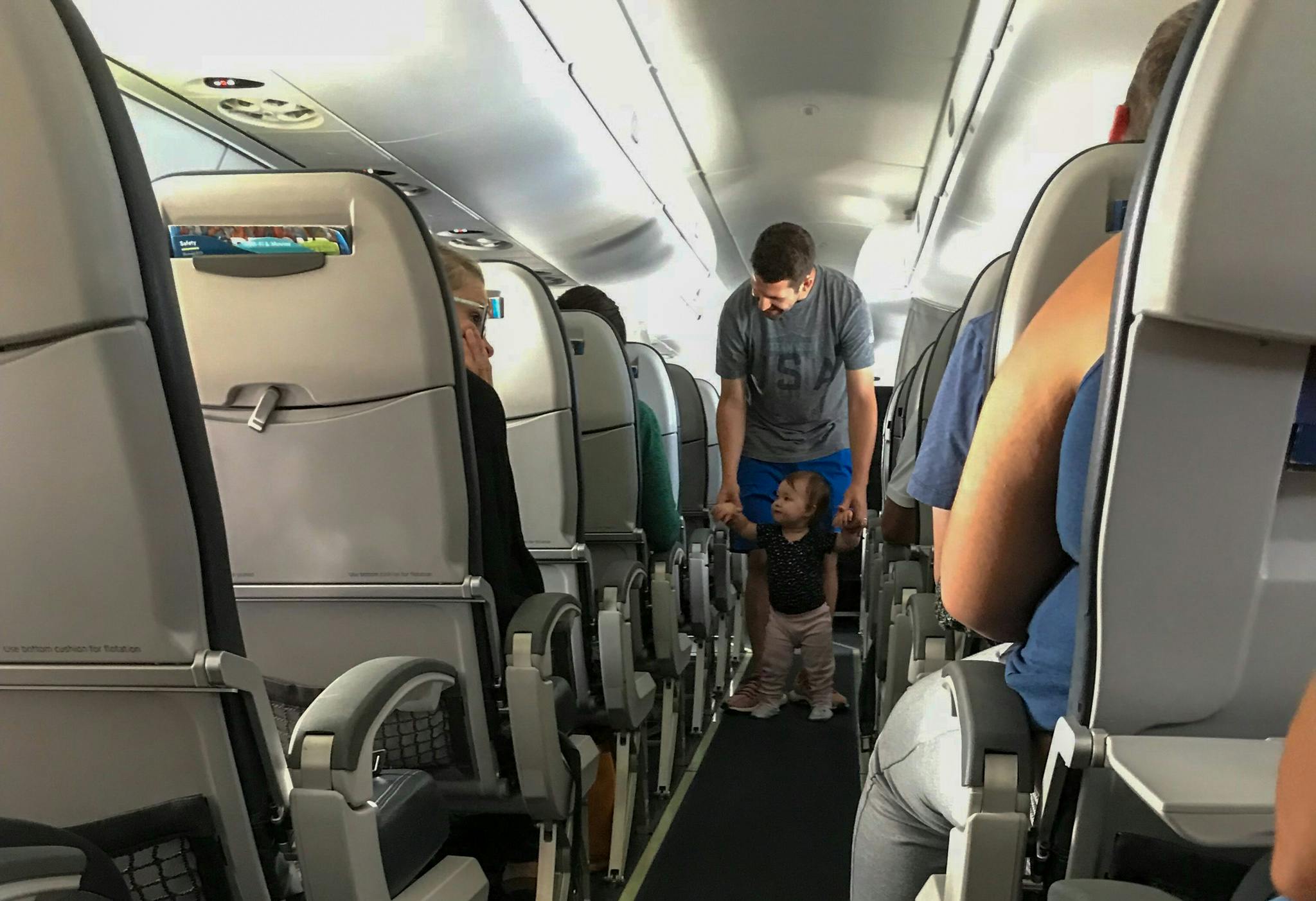 a man helping a small child walk down plane aisle