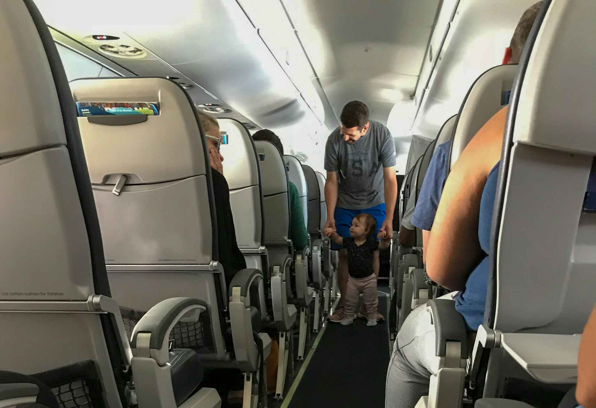A father walking his child down the aisle of an airplane.