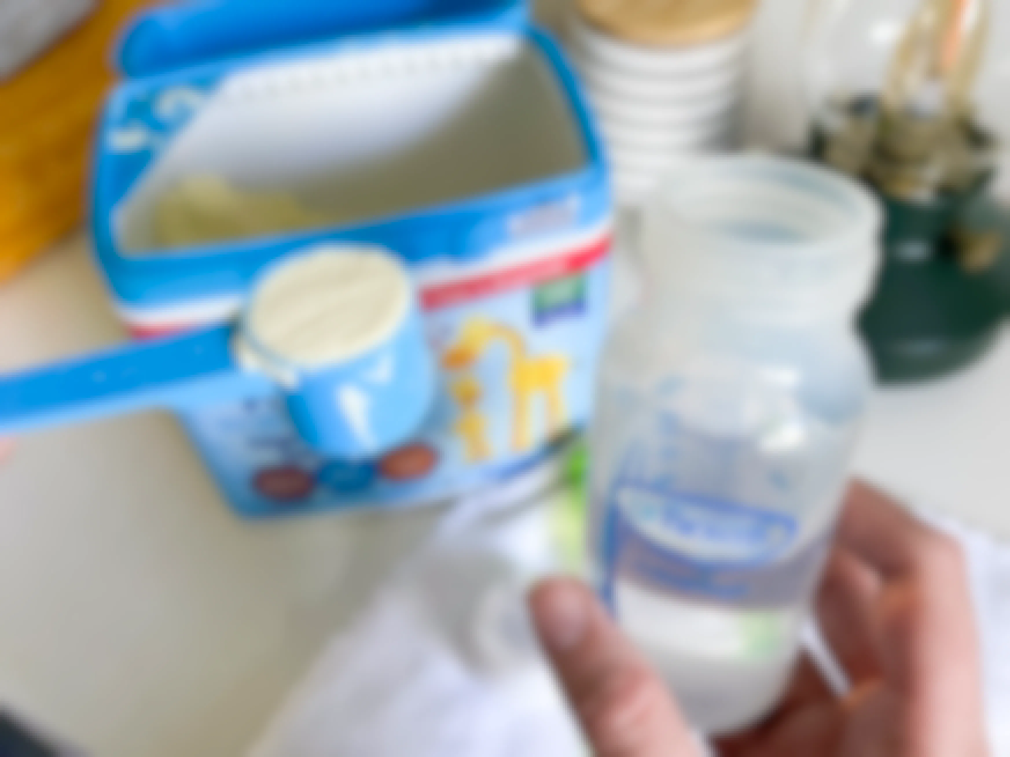 A person putting a scoop of Kirkland powdered baby formula into a bottle.