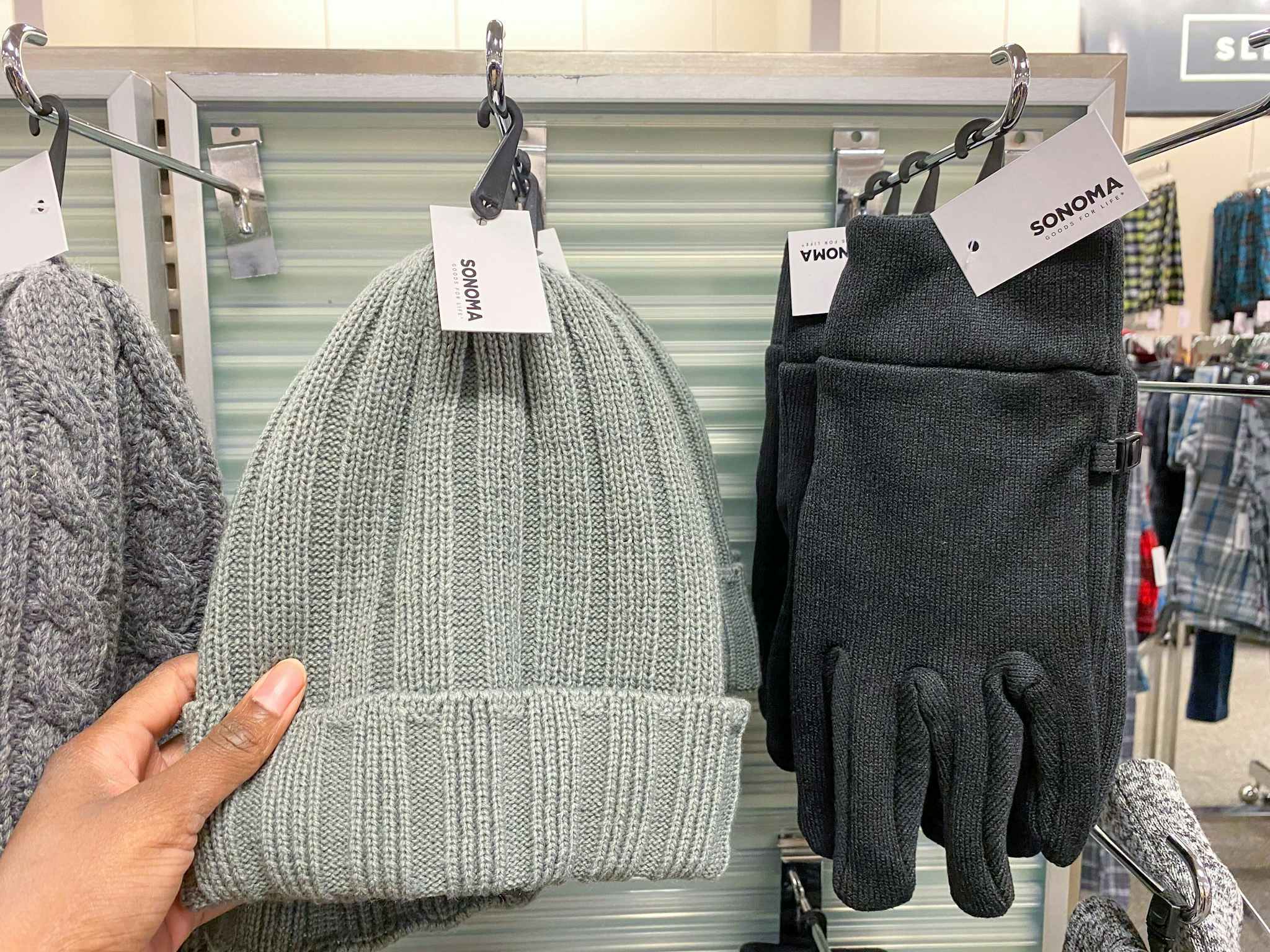 A person's hand taking a beanie from a display of winter hats and gloves in Kohl's.