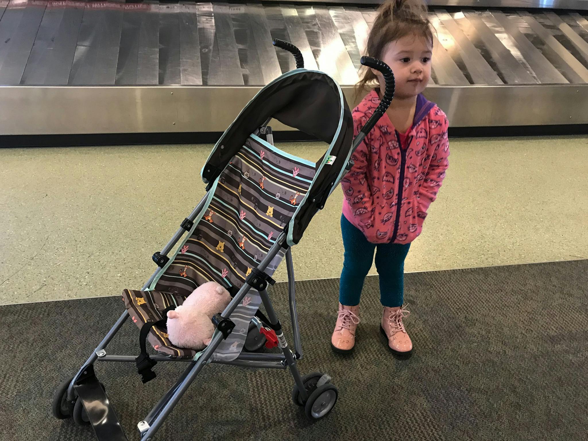 a little girl standing next to stroller at baggage claim