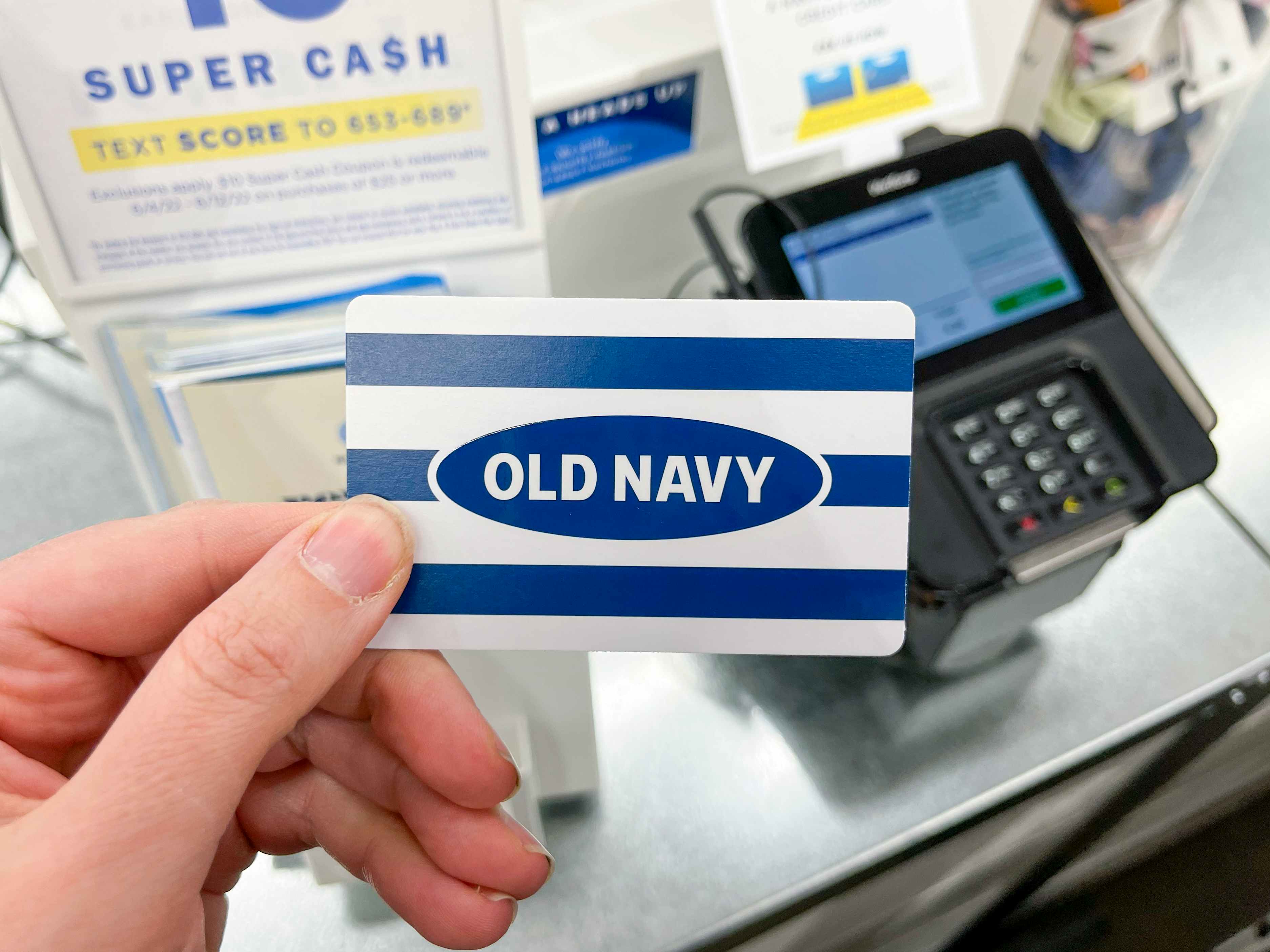 A white and blue Old Navy gift card held near the checkout register.
