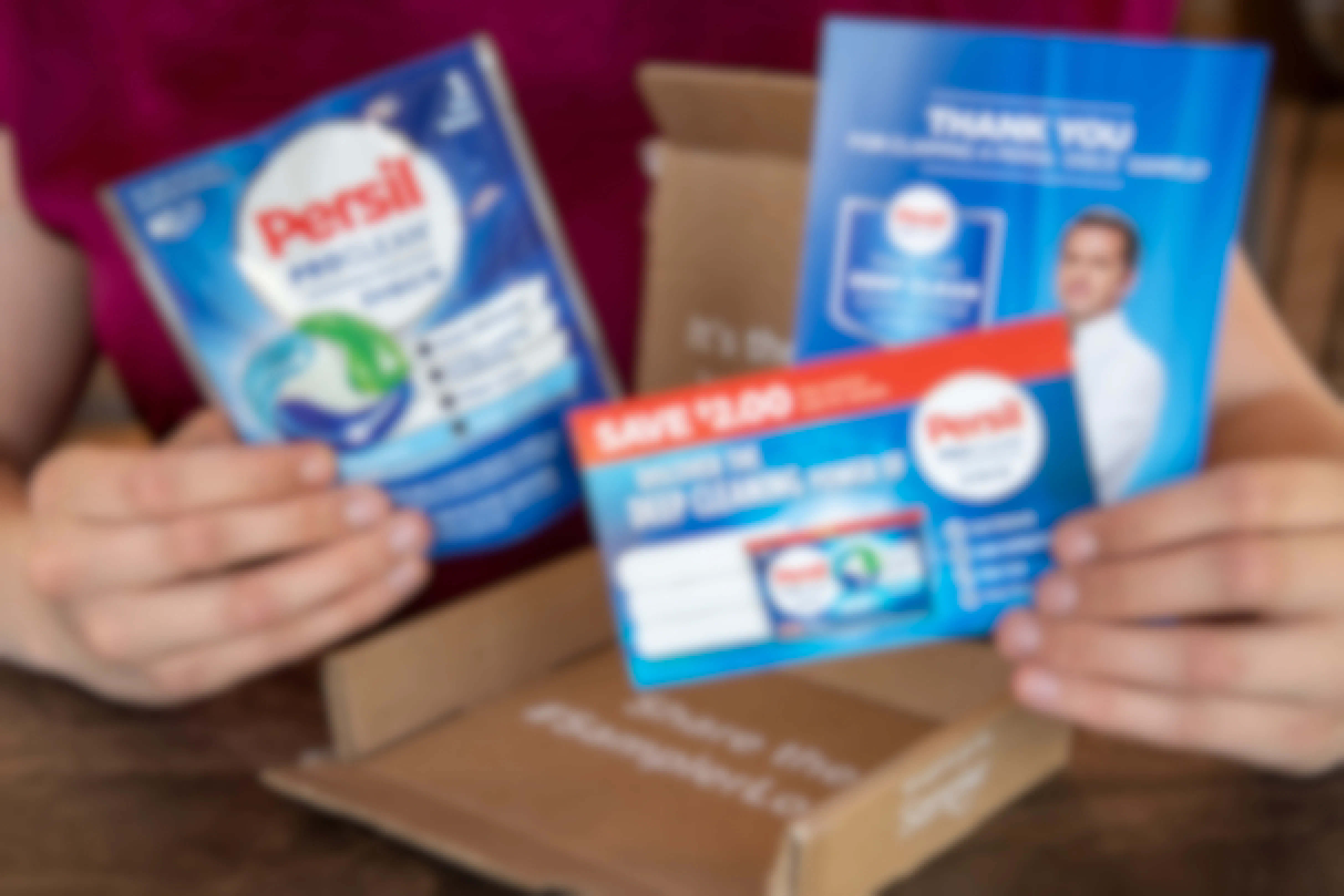 A woman holding a Persil sample with a coupon and info advertisement next to the Sampler box they came in.