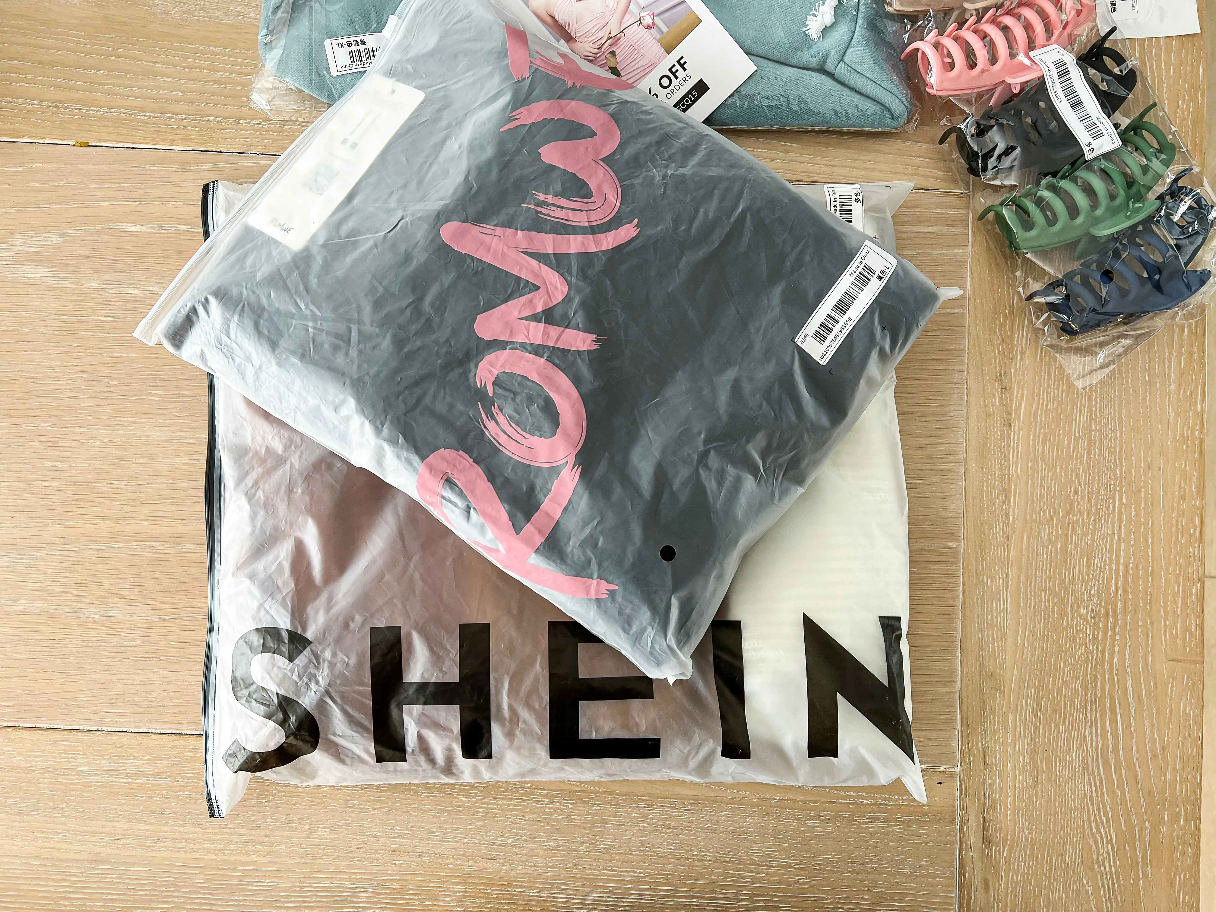 Plastic bags from Shein and Romwe stacked on a wooden table next to some hair clips.