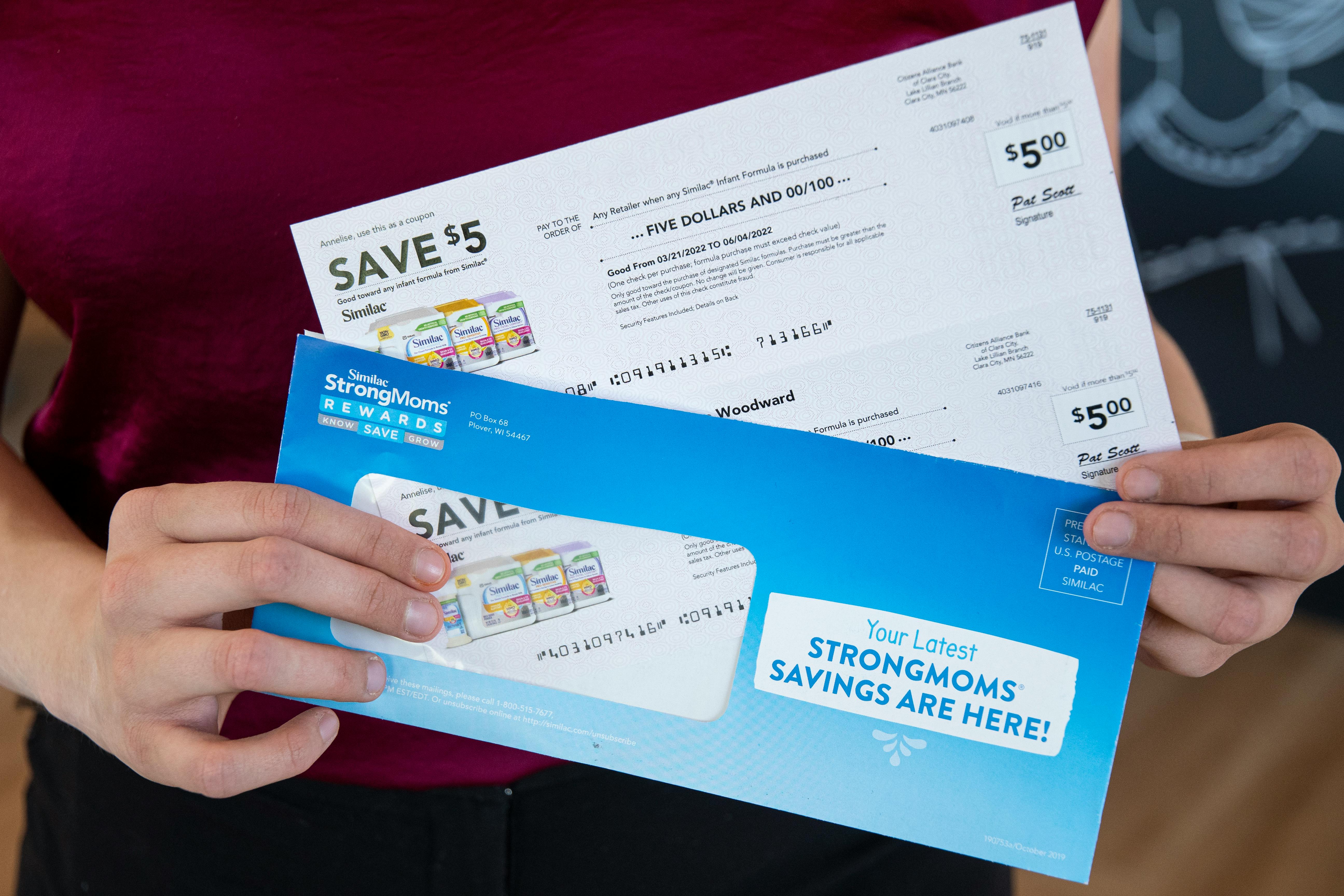 A woman holding an envelope, pulling two Similac baby formula coupons from it.