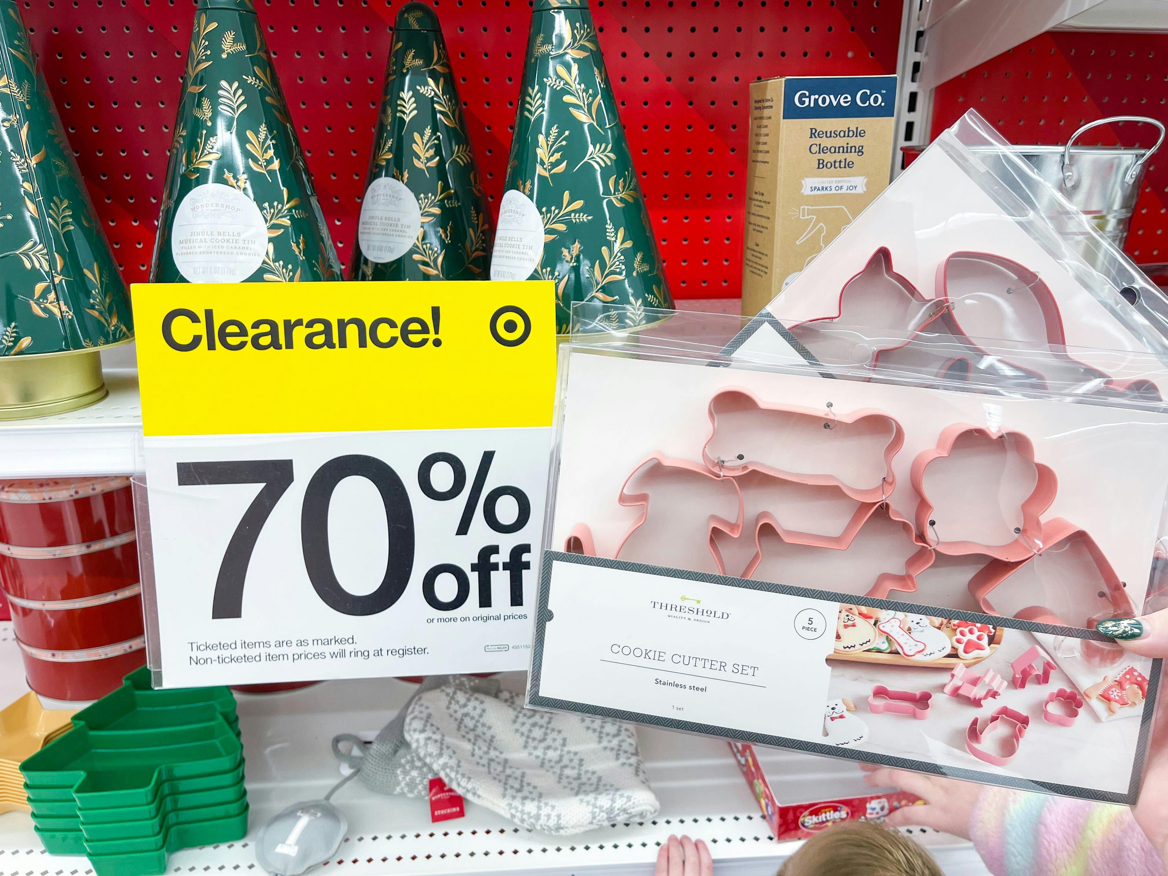 A box of Christmas cookie cutters being held up next to a Target clearance sign for 70% off on a shelf with more Christmas decor.