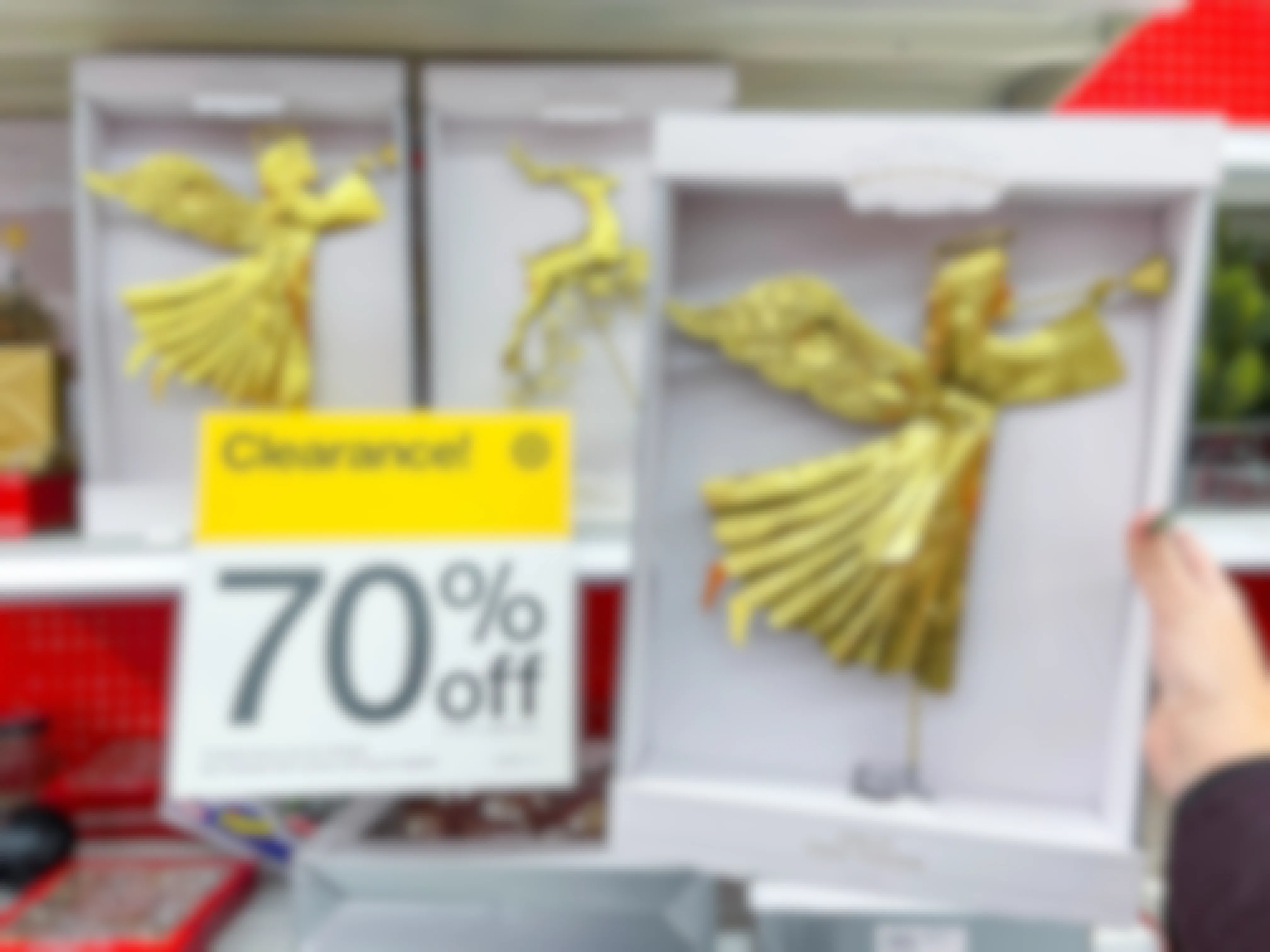 A person's hand holding up a Wondershop Christmas tree topper next to a sign that reads, "Clearance 70% off" on a shelf of Christmas decor at Target.