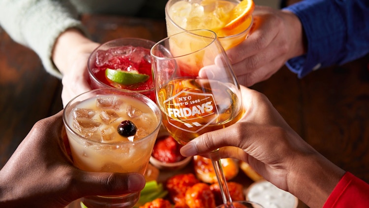 4 people clinking beverages. One of the glasses as a TGI Fridays logo on it.