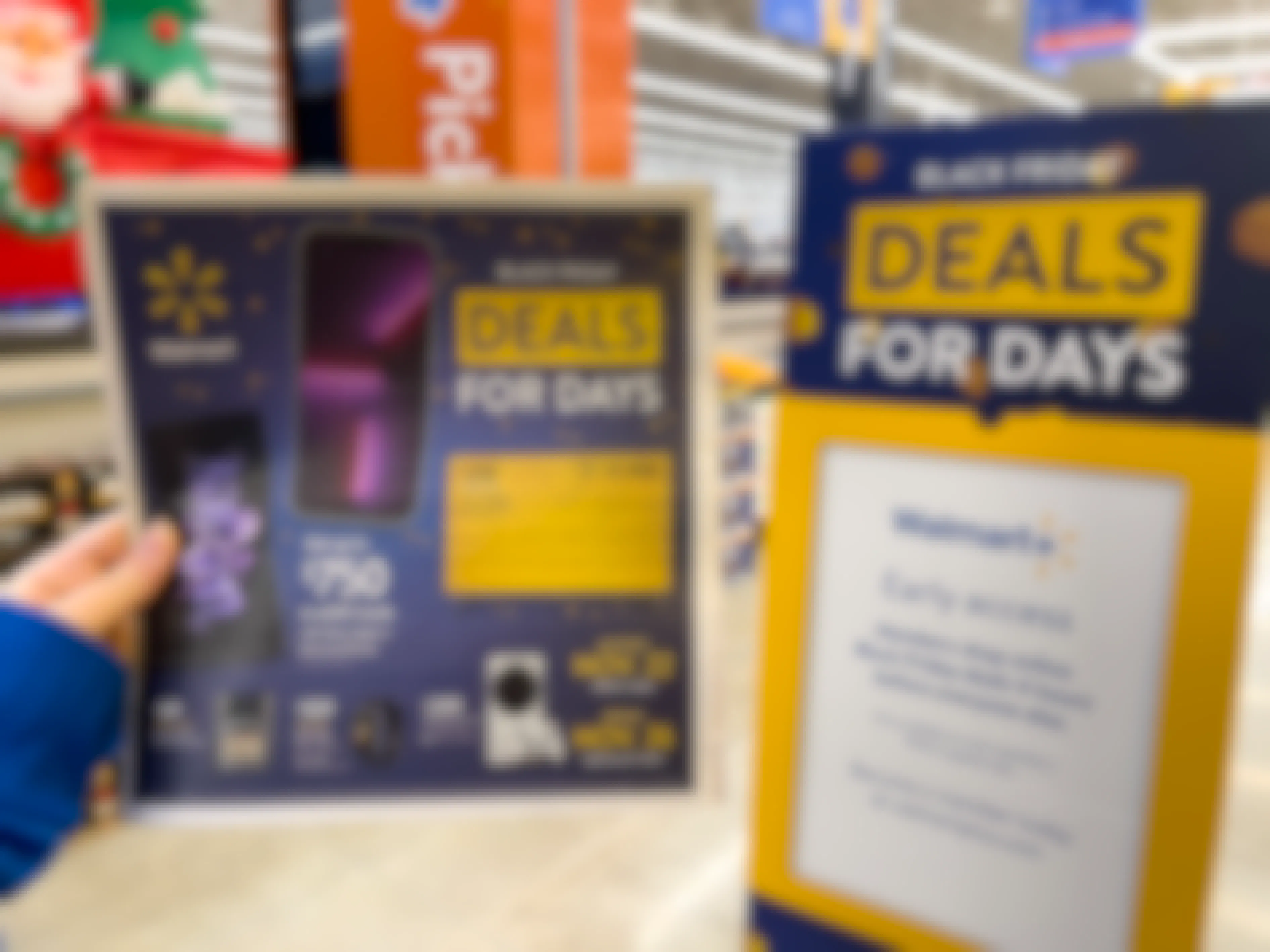 A person's hand holding up the Walmart Black Friday paper ad next to a Deals for Days sign inside Walmart.