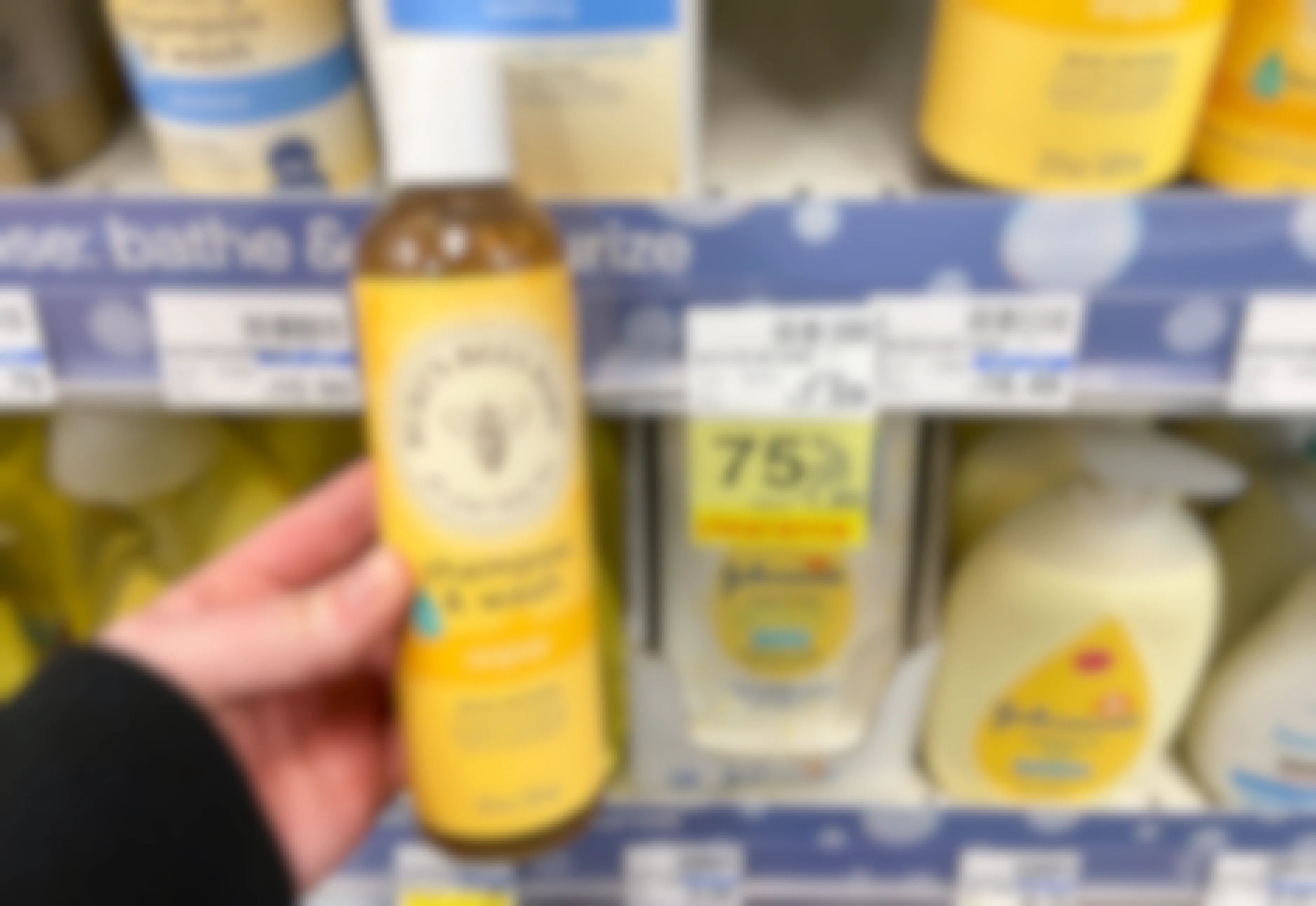 A person's hand holding a bottle of Burt's Bees Baby shampoo & Wash in front of a shelf at CVS.