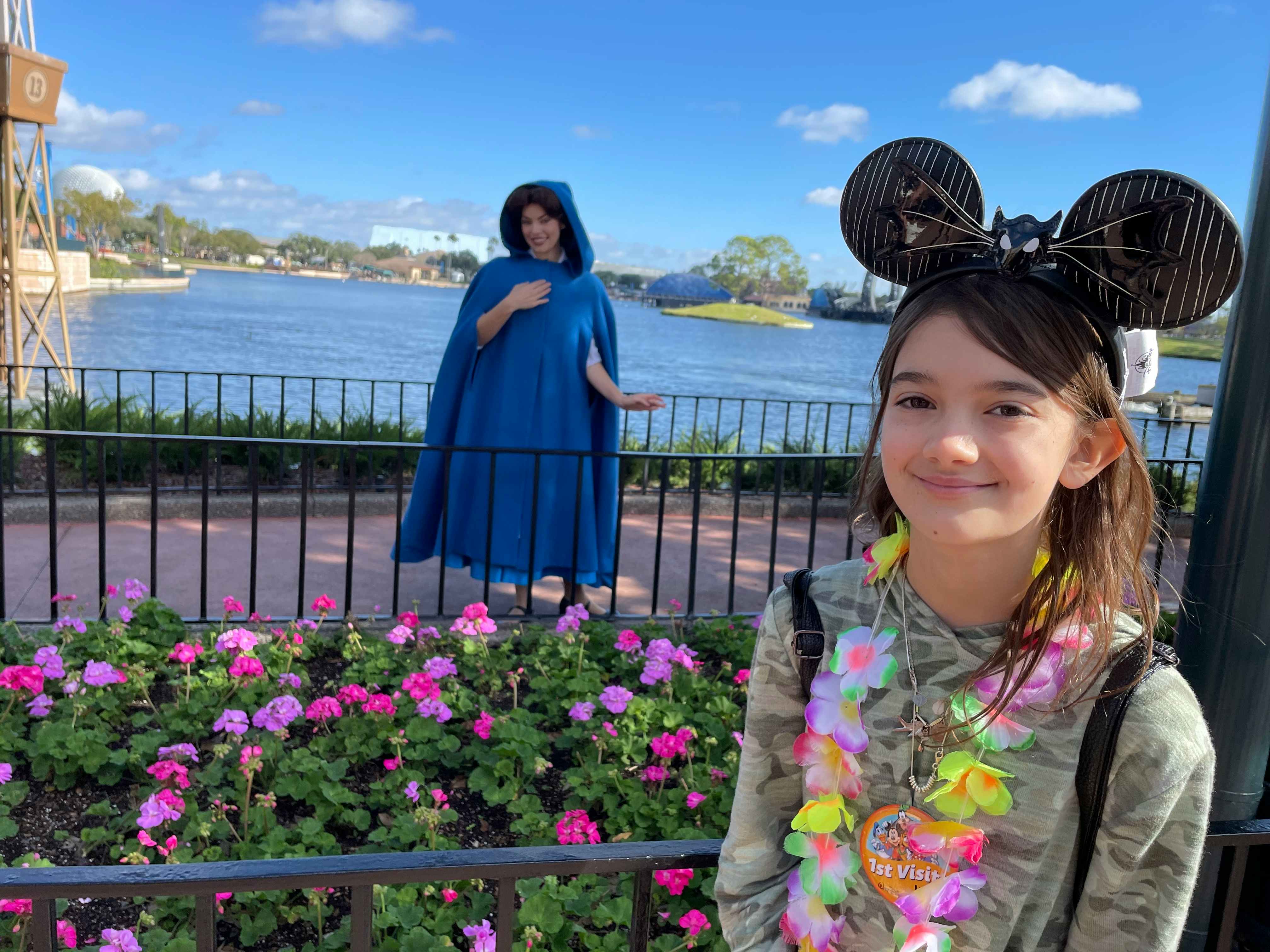 A child standing near a garden with Princess Belle in the background at Disney World.