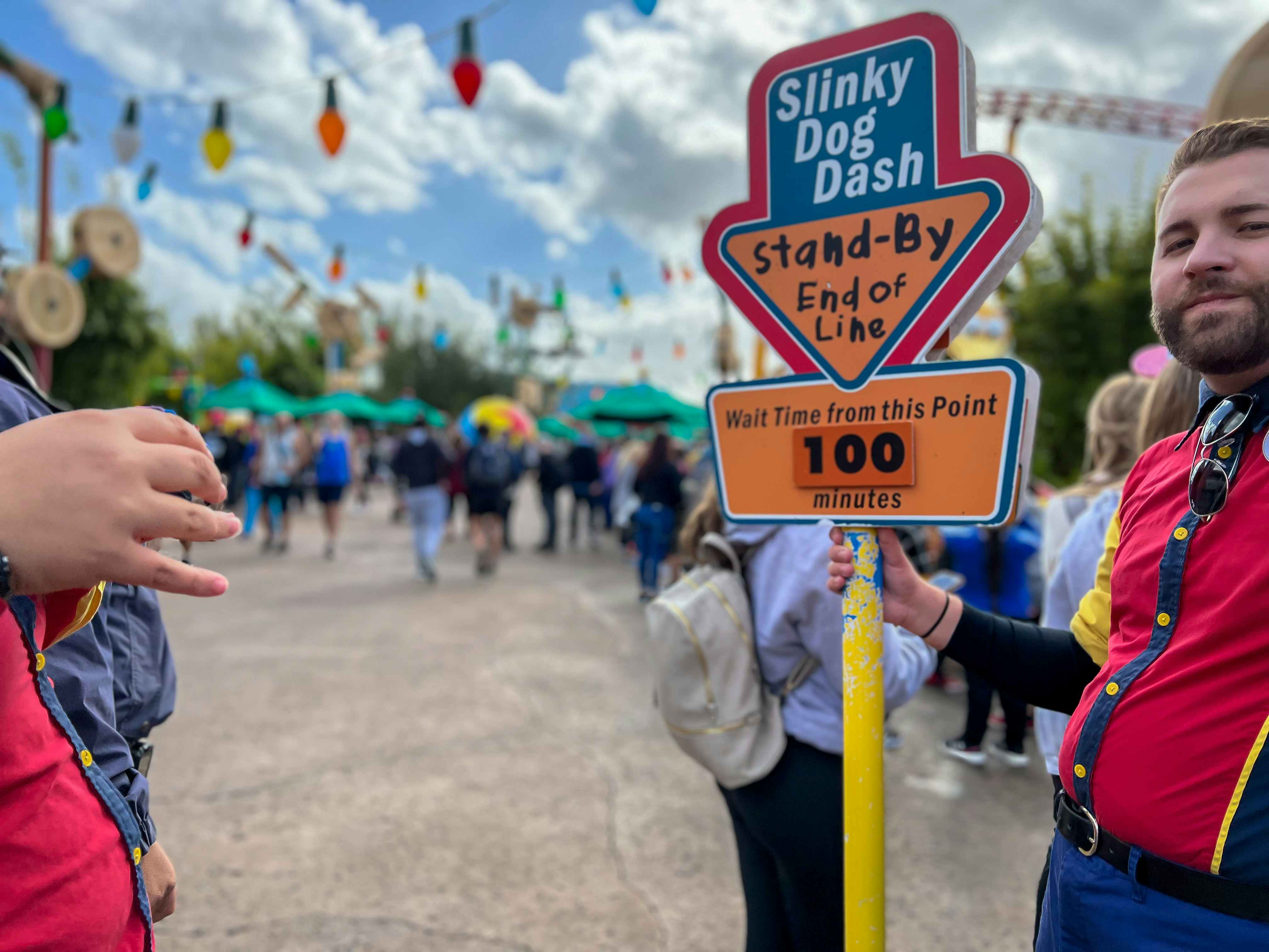 A Disney employee holding a sign for the Slinky Dog Dash ride, indicating that the wait time from that point is 100 minutes.