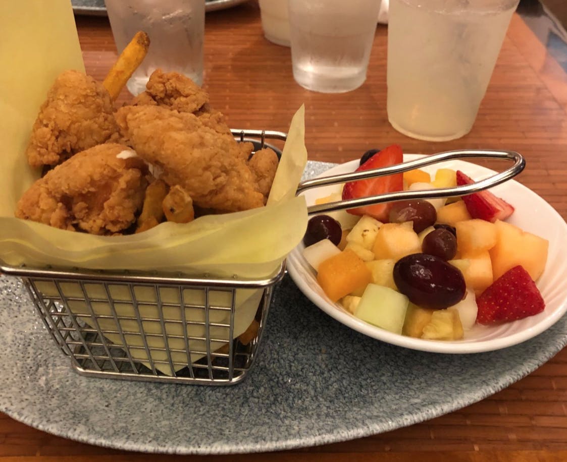 A Disneyland kids meal consisting of a basket of chicken tenders and a small bowl of mixed fruit.