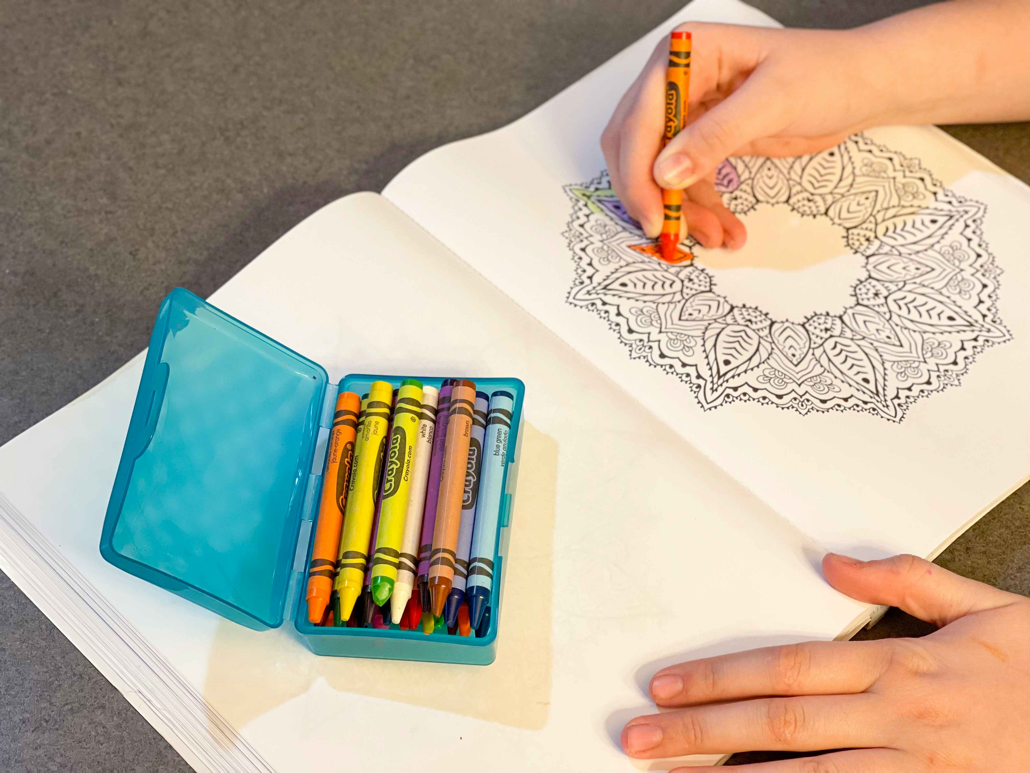 someone drawing in a coloring book with crayons stored in soap case 