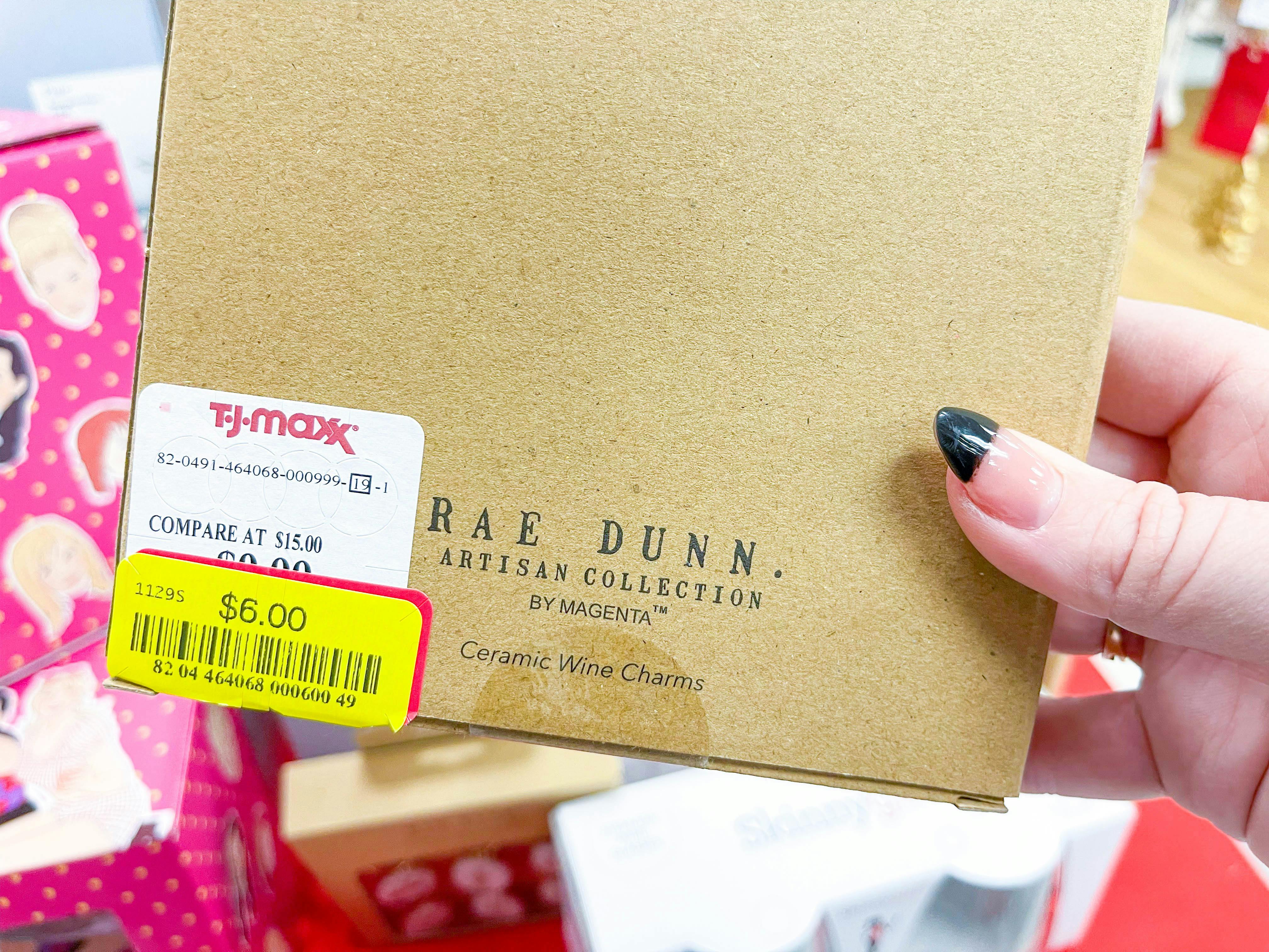 A person's hand holding a Rae Dunn by Magenta product with a clearance sticker.