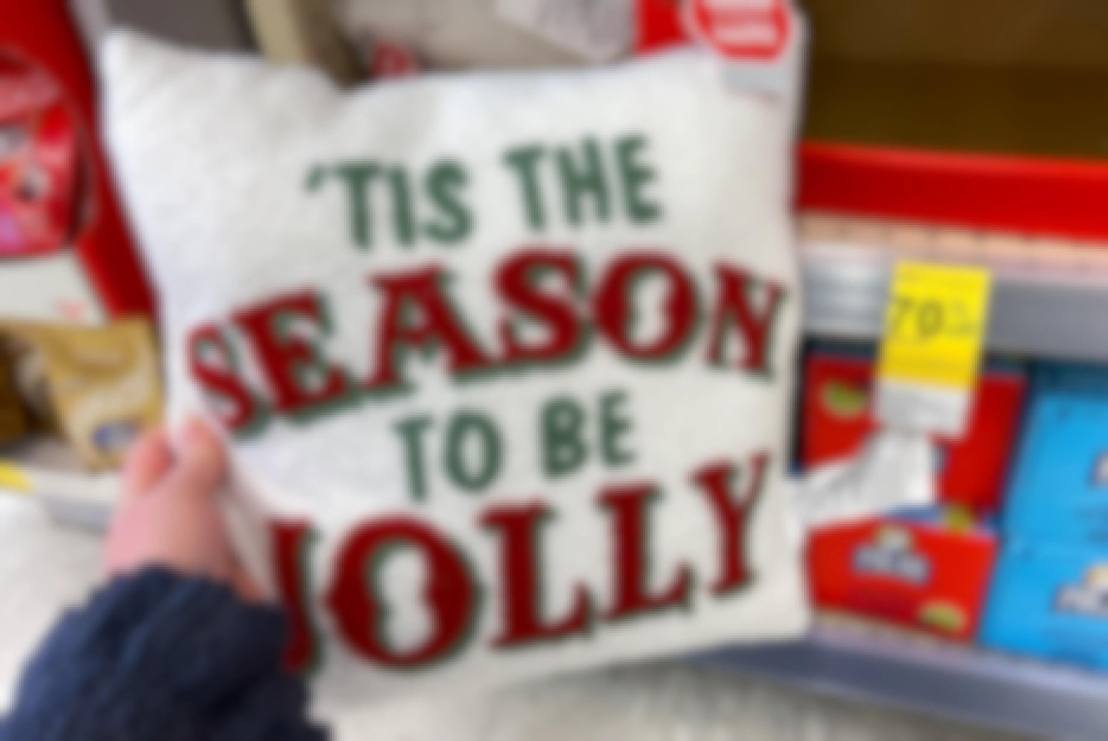 A person holding a pillow that says 'Tis the season to be jolly.