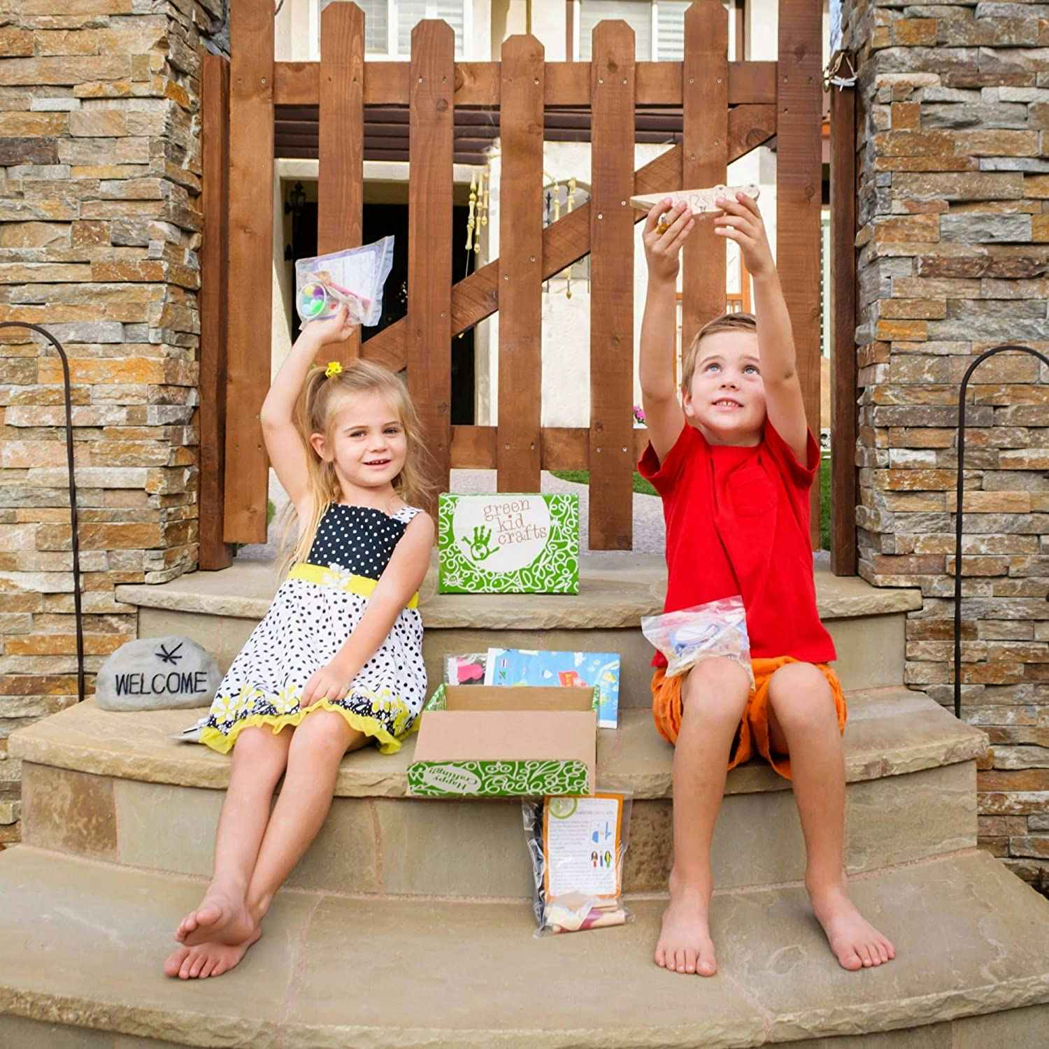 Two kids holding up crafts on a front stoop 