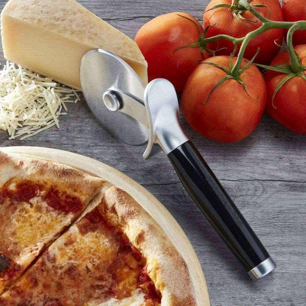 A pizza cutter near a pizza, tomatoes, and cheese.
