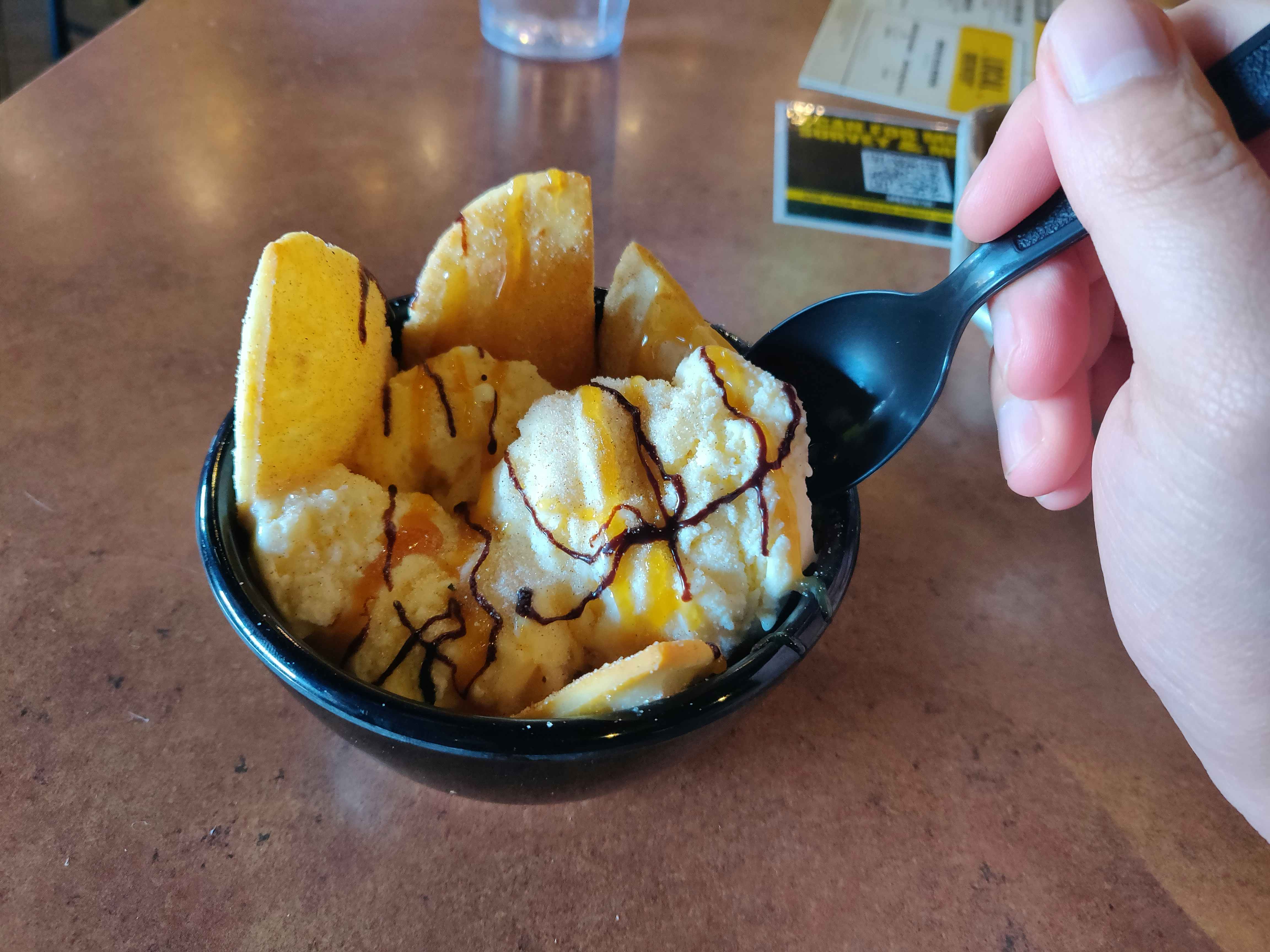 A person scooping their spoon into a bowl of Buffalo Wild Wings loaded ice cream sitting on the table.