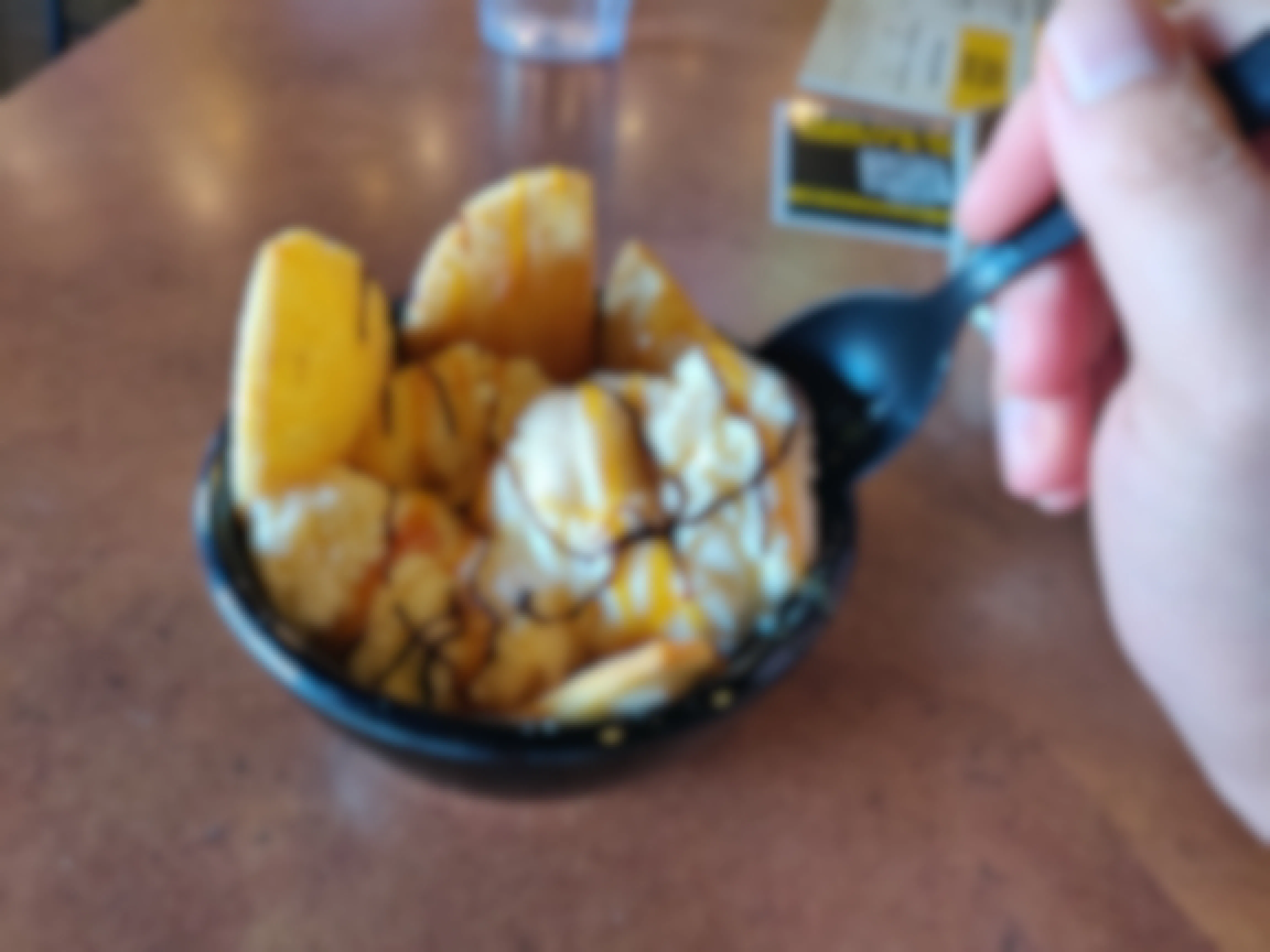 A person scooping their spoon into a bowl of Buffalo Wild Wings loaded ice cream sitting on the table.