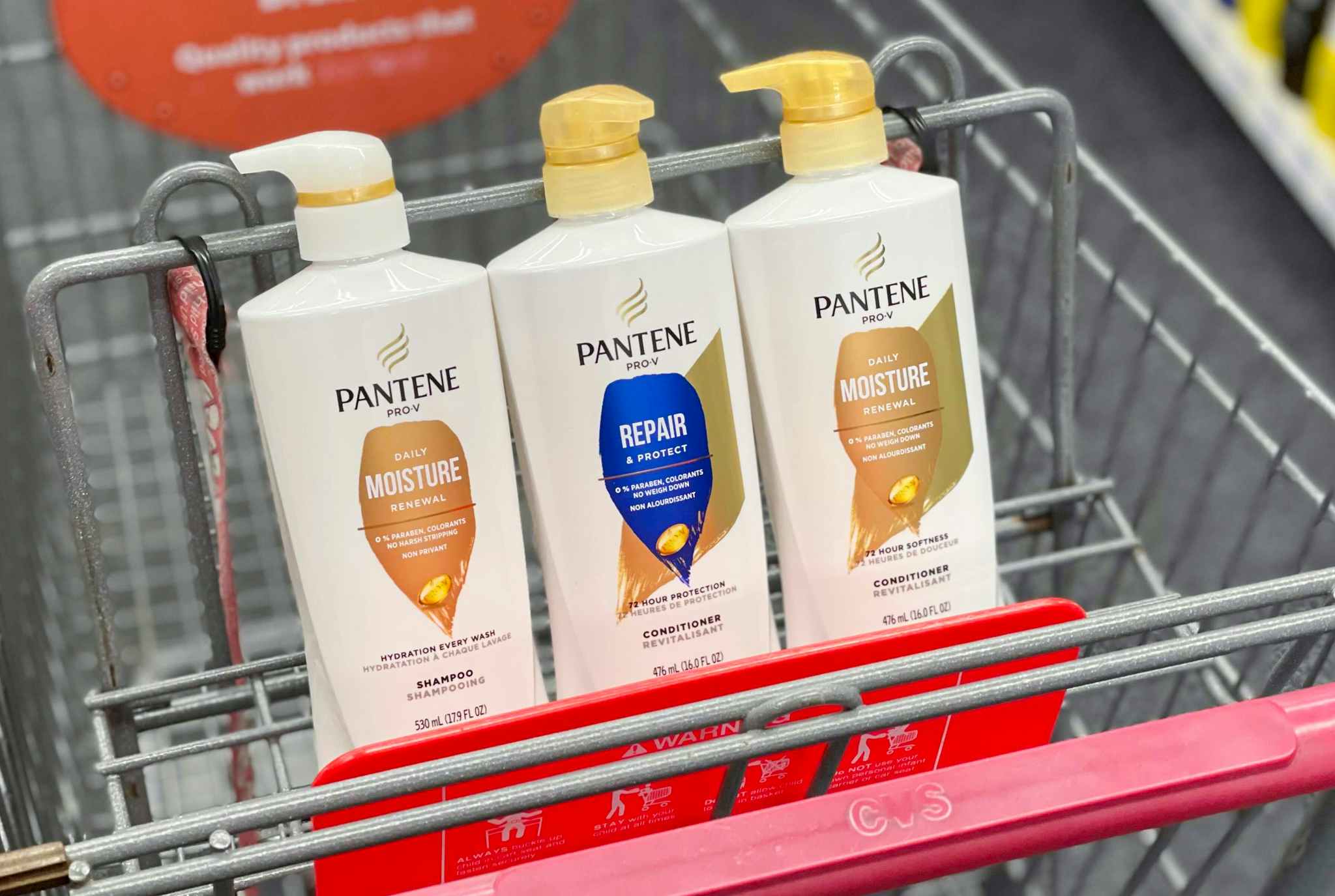 Three bottles of Pantene hair products sitting in the basket of a shopping cart at CVS.