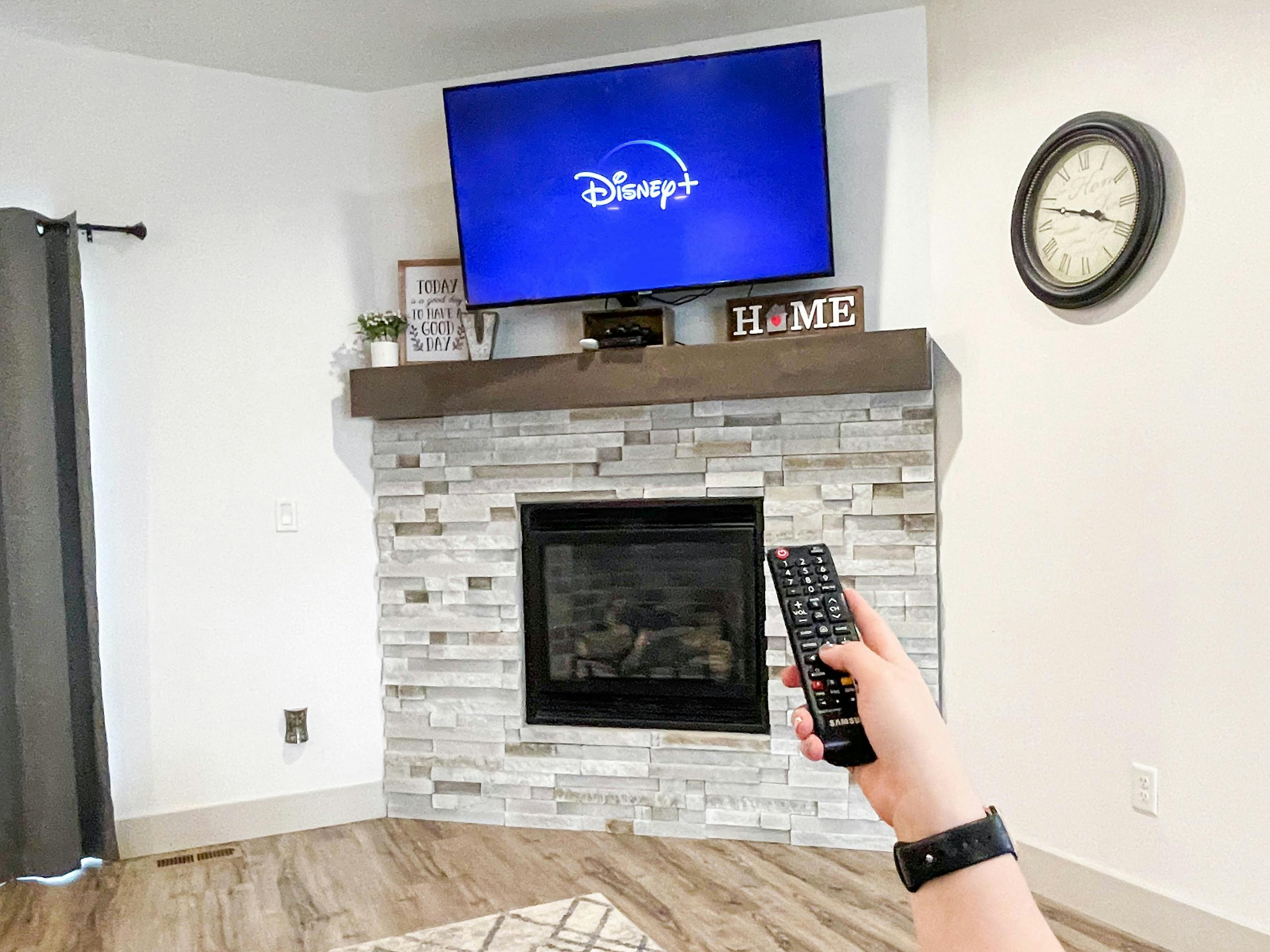 A person pointing a remote at a TV that is starting the Disney+ app