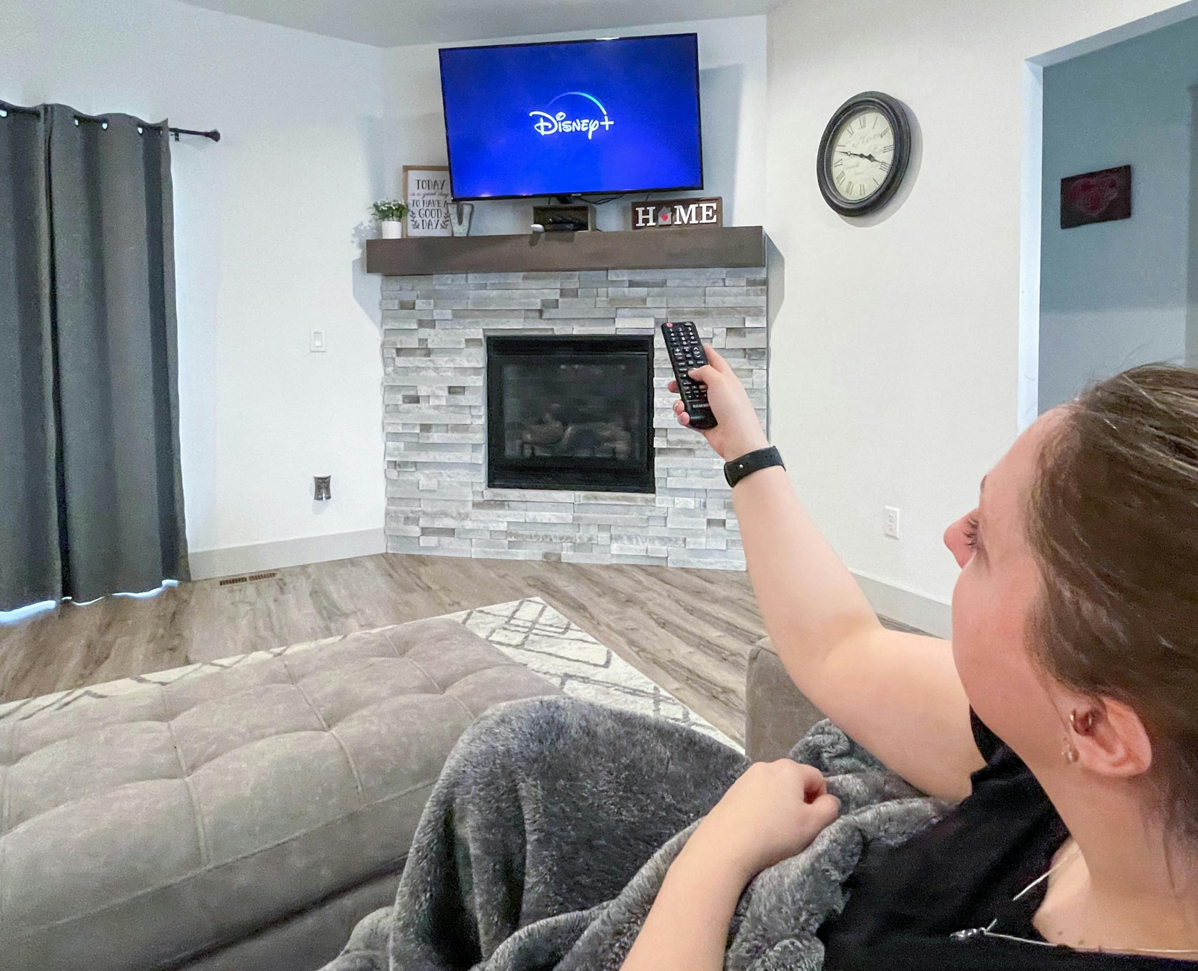 woman pointing remote to tv with disney plus loading